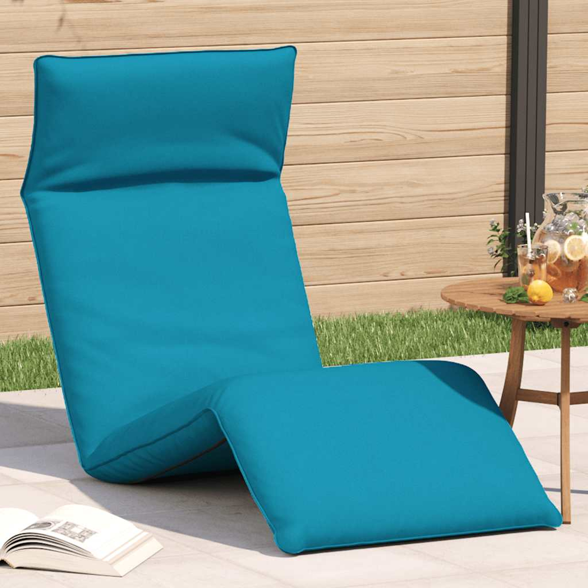 Chaise longue verde acqua su patio con recinzione in legno, erba e tavolino con bevande.