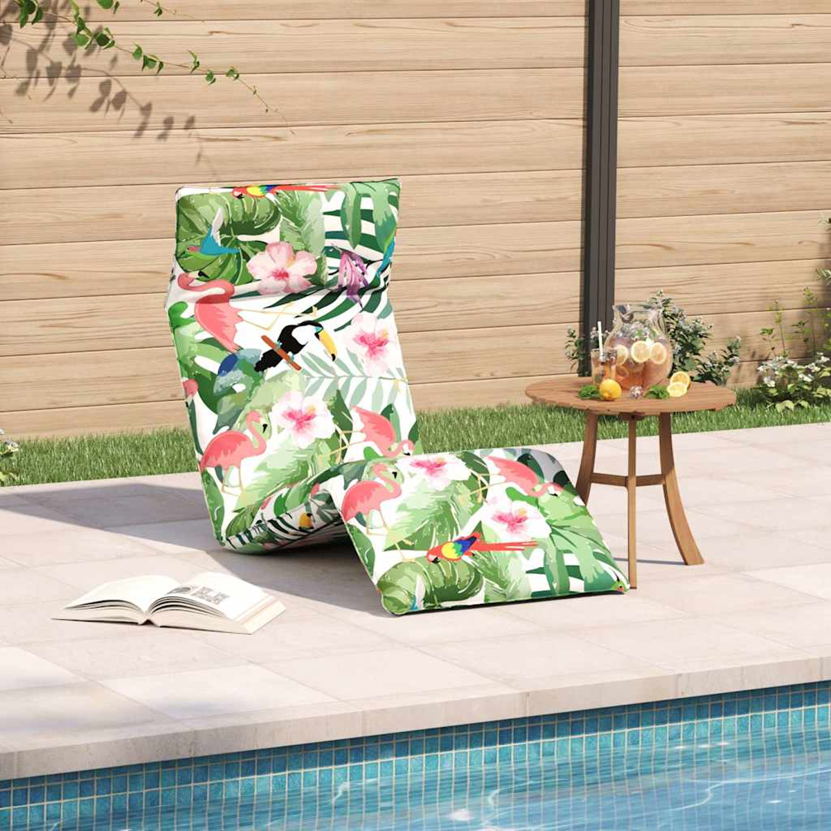 Una sdraio e un cuscino con stampa tropicale vicino a una piscina, con tavolo e brocca nelle vicinanze.