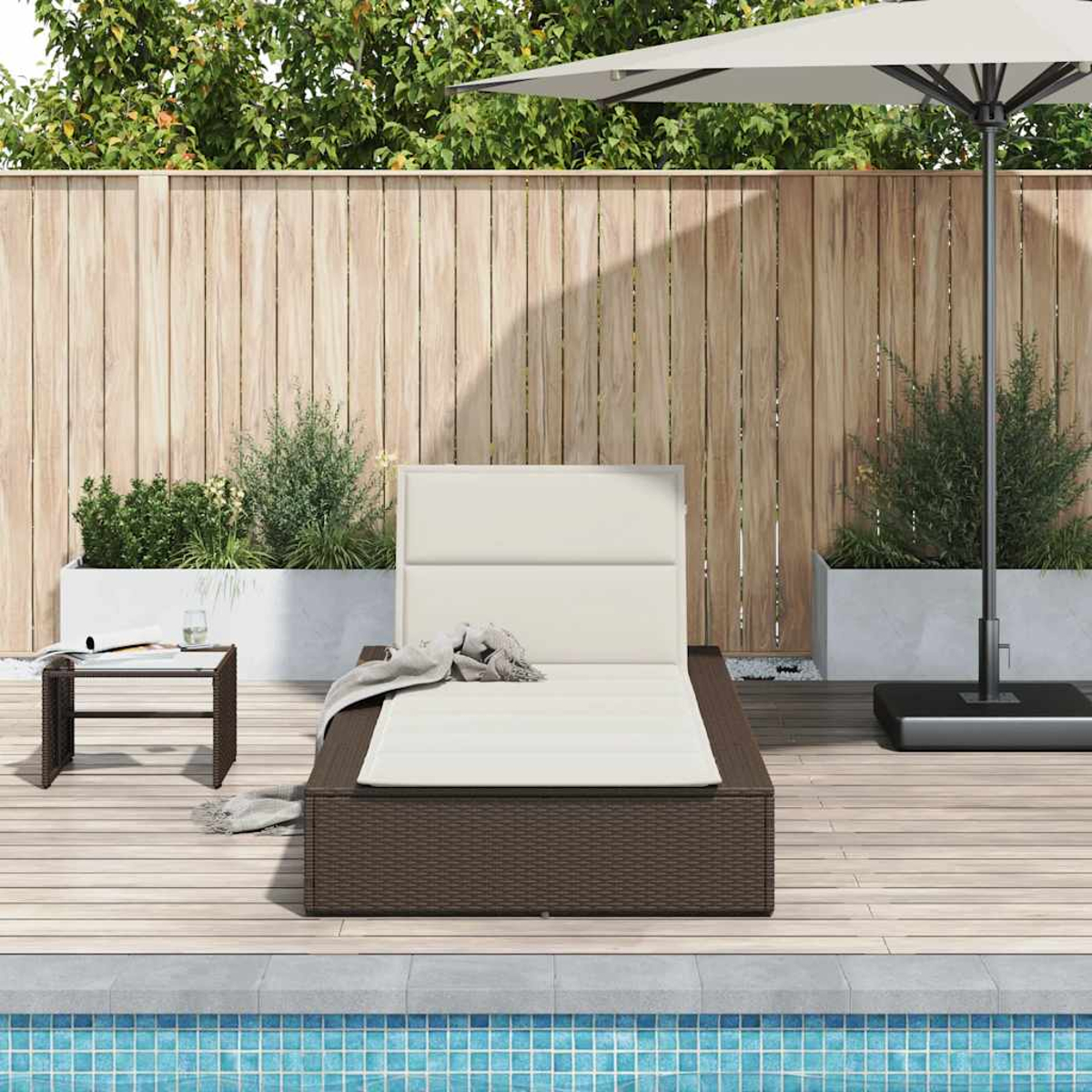 Lettino prendisole in rattan marrone con cuscino bianco, tavolino e ombrellone vicino alla piscina.