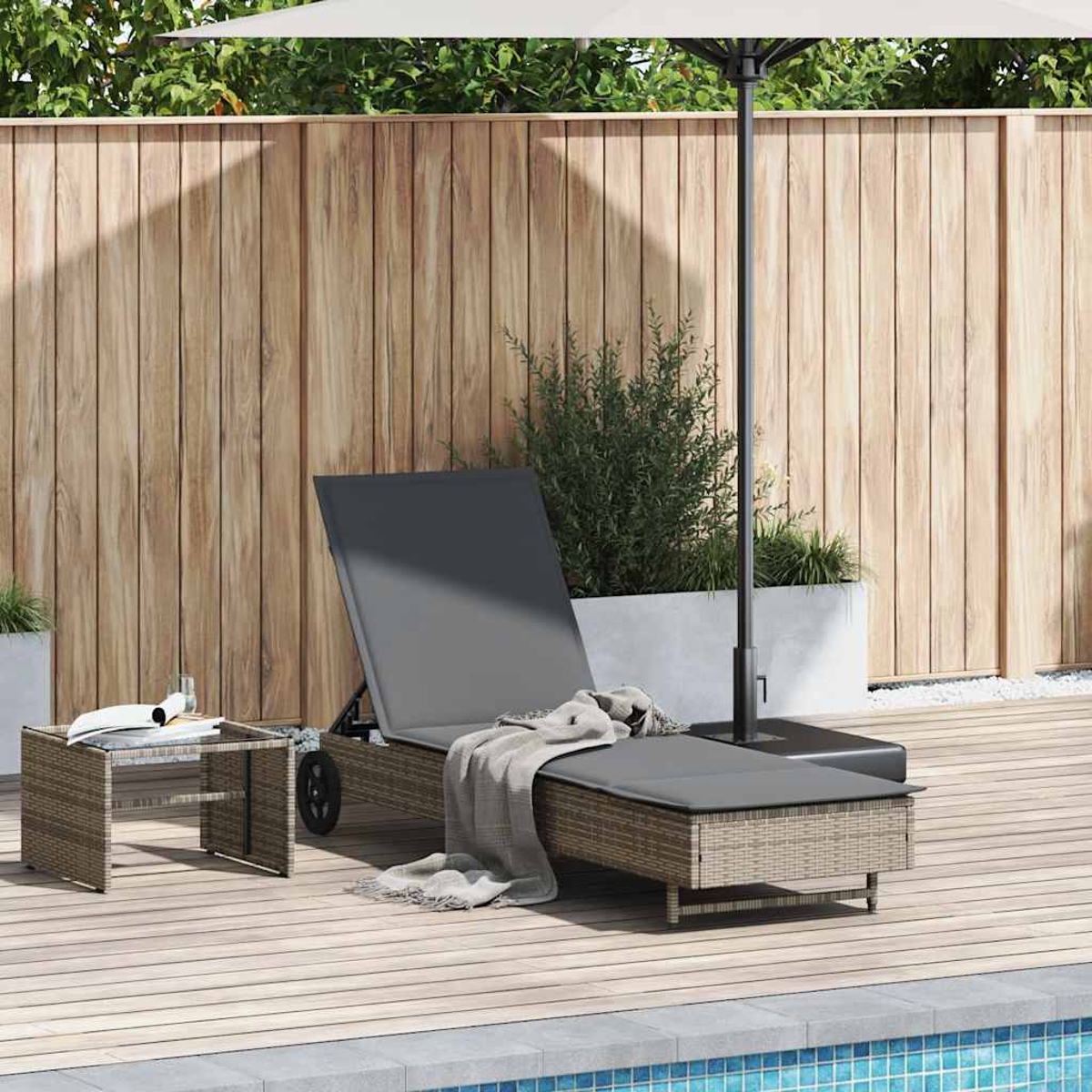 Una sedia a sdraio con cuscino e coperta, un tavolo e un ombrellone su una terrazza di legno vicino a una piscina.