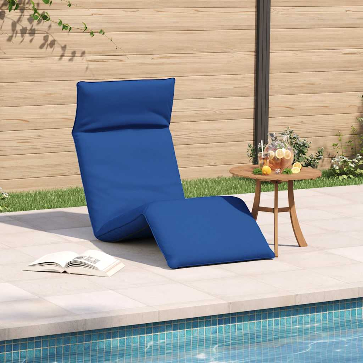 Blaue Liege neben einem Tisch mit Getränk und einem Buch am Pool.