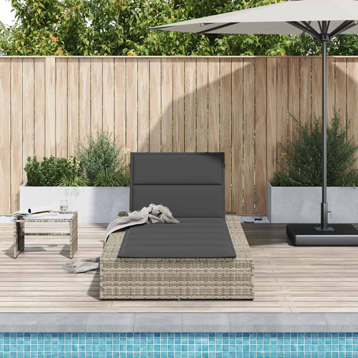 Lettino grigio con coperta su terrazza in legno vicino piscina, con recinzione e piante.