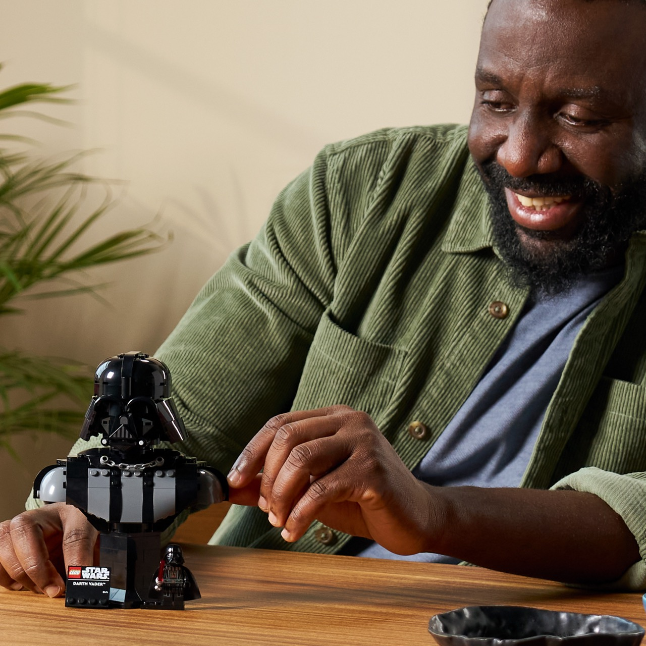 Uomo gioca con busto e minifigure LEGO di Darth Vader, camicia verde in velluto a coste.