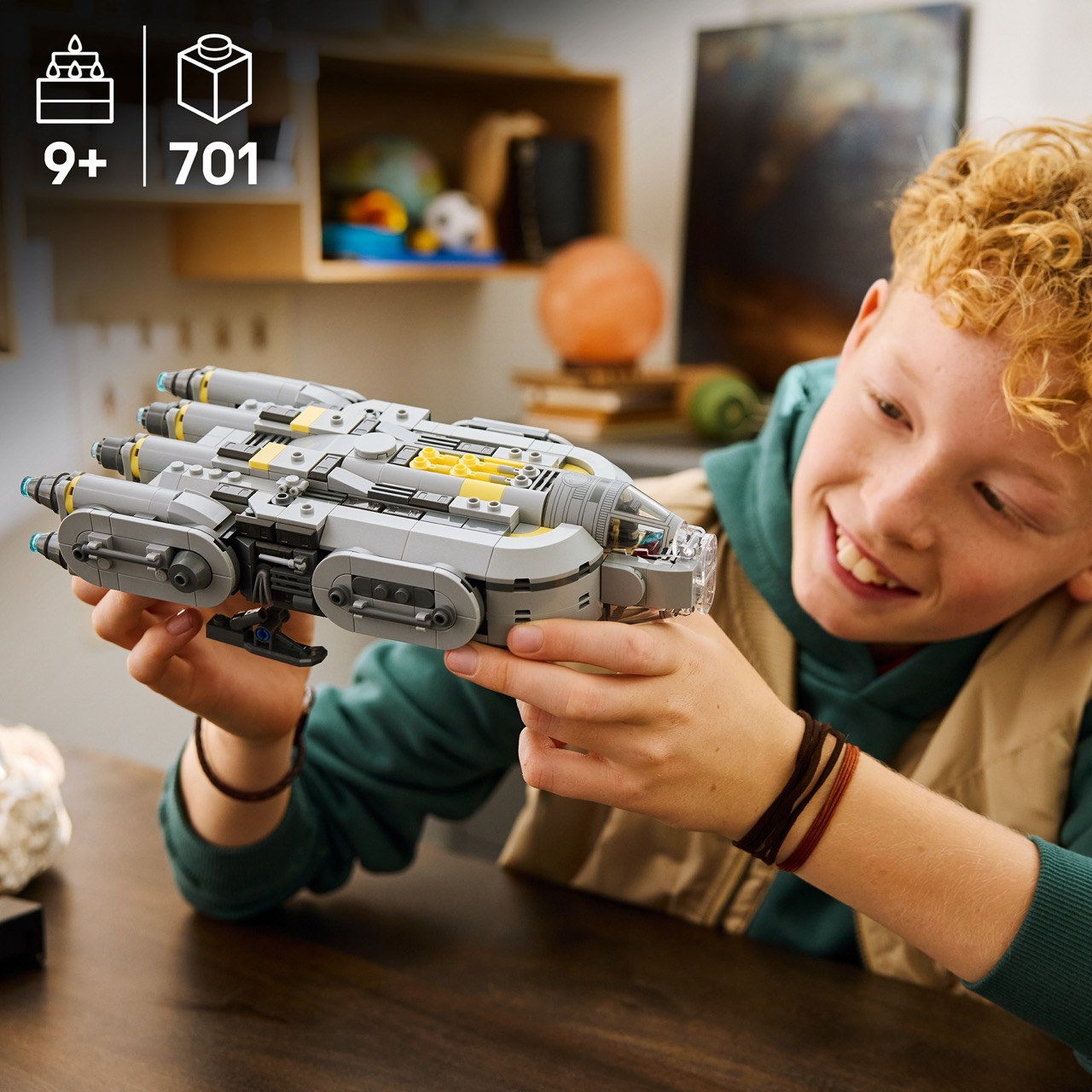 Çocuk Lego uzay gemisi tutuyor, yaş 9+, 701 parça. Raflı arka plan.