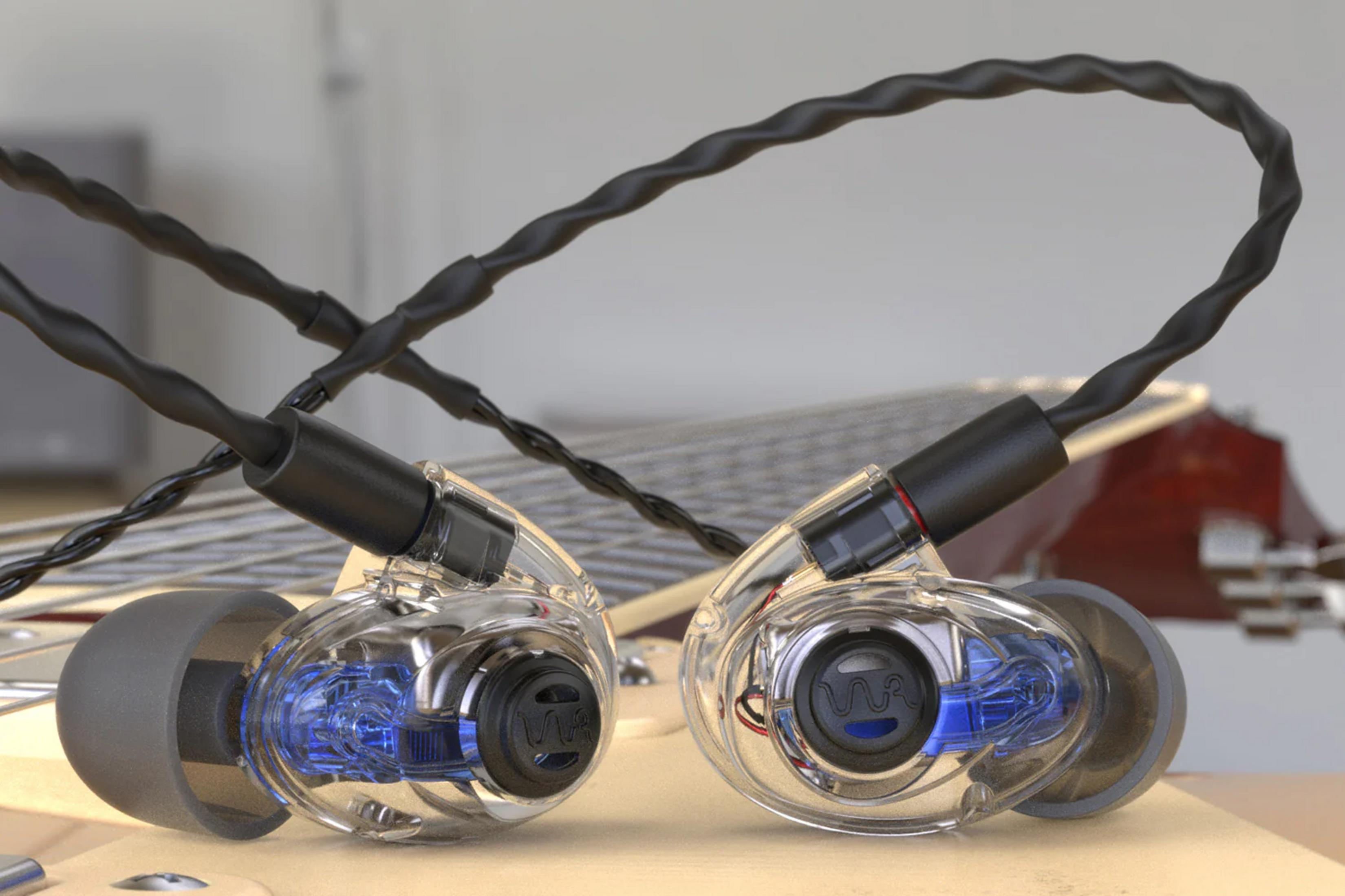 Transparente Ohrhörer mit blauen Elementen und schwarzen Kabeln auf einer Gitarre.