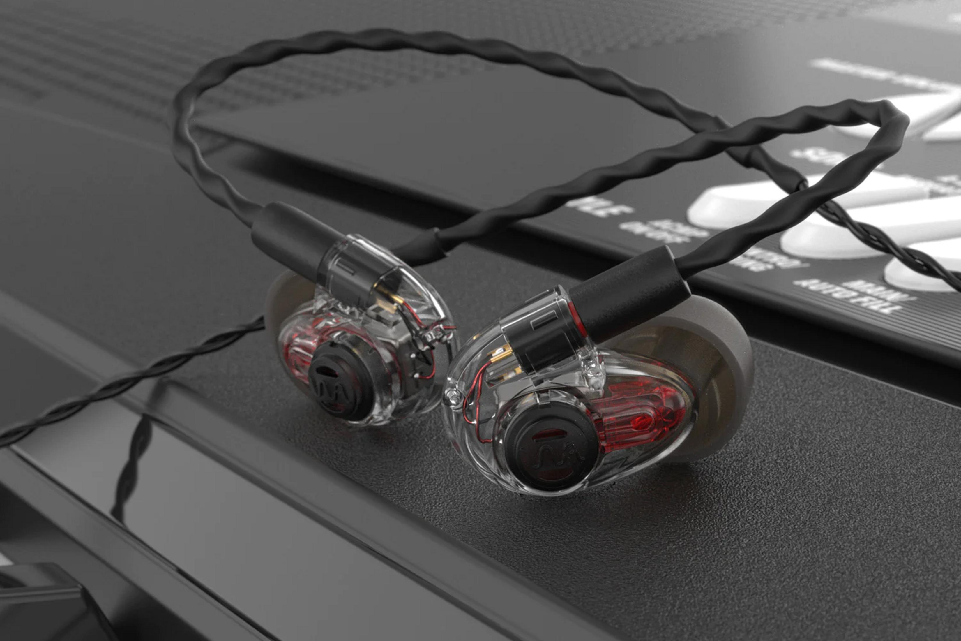 Transparente In-Ear-Monitore mit roten Akzenten und schwarzen Kabeln auf texturierter Oberfläche.