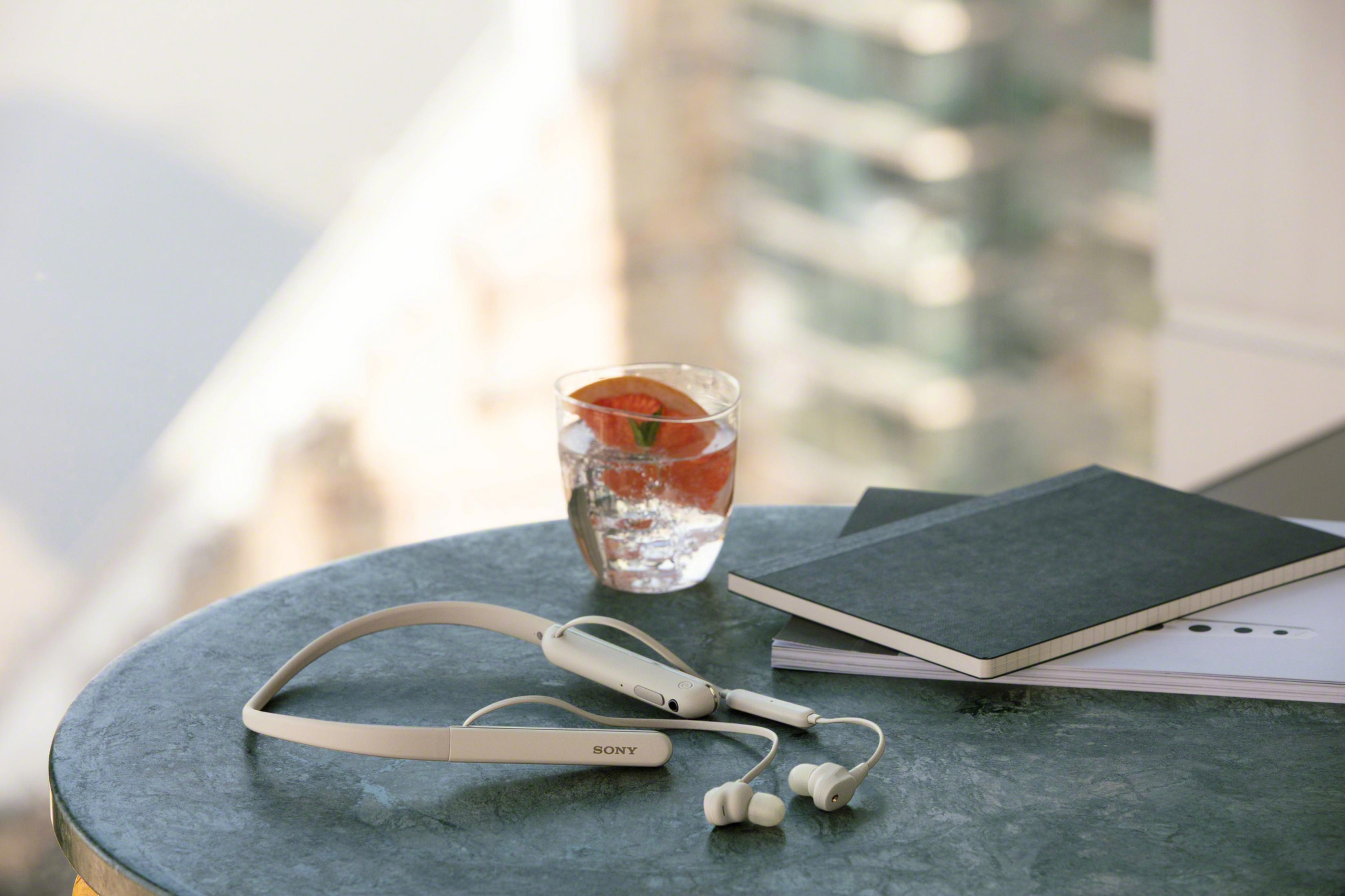 White headphones rest near a glass of water with grapefruit on a table.