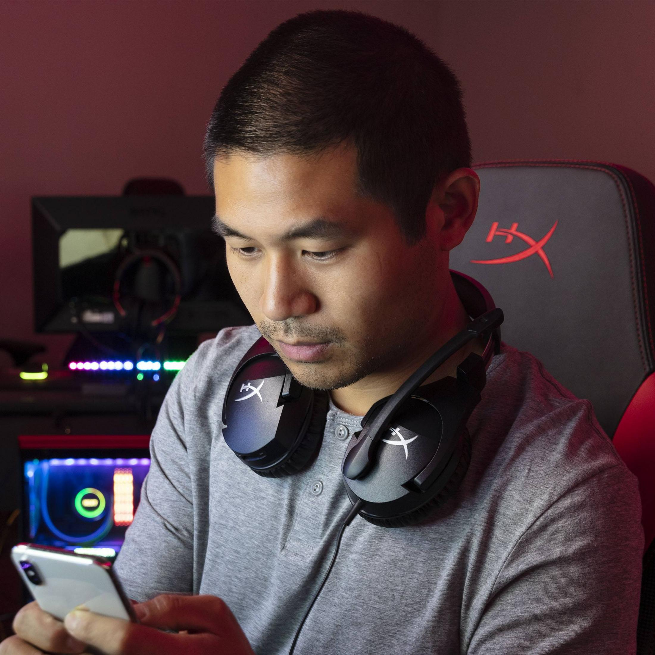 Hombre con auriculares en escritorio, mirando un smartphone.