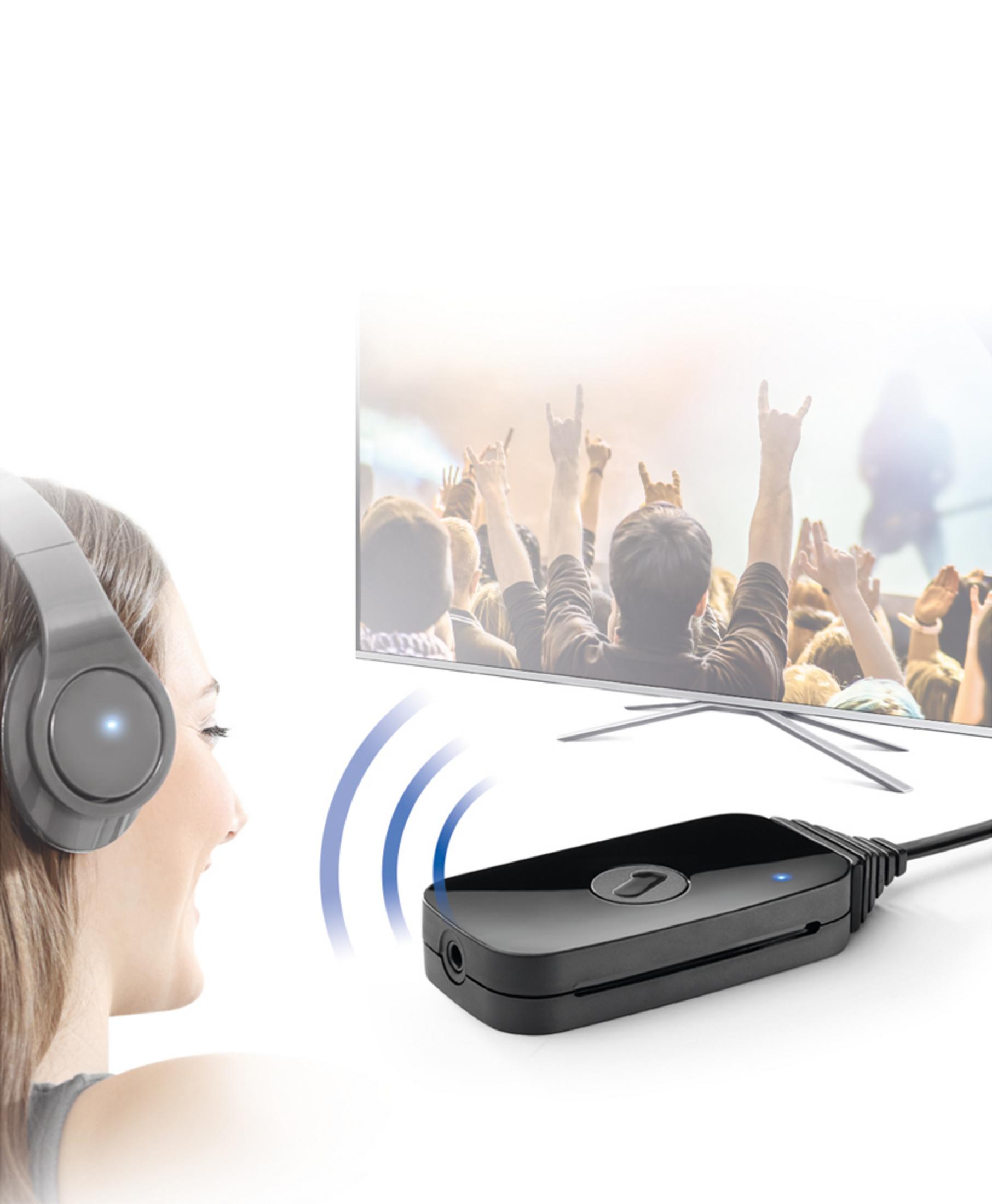 Mujer con auriculares mira TV con multitud animando. Se ve un transmisor negro.