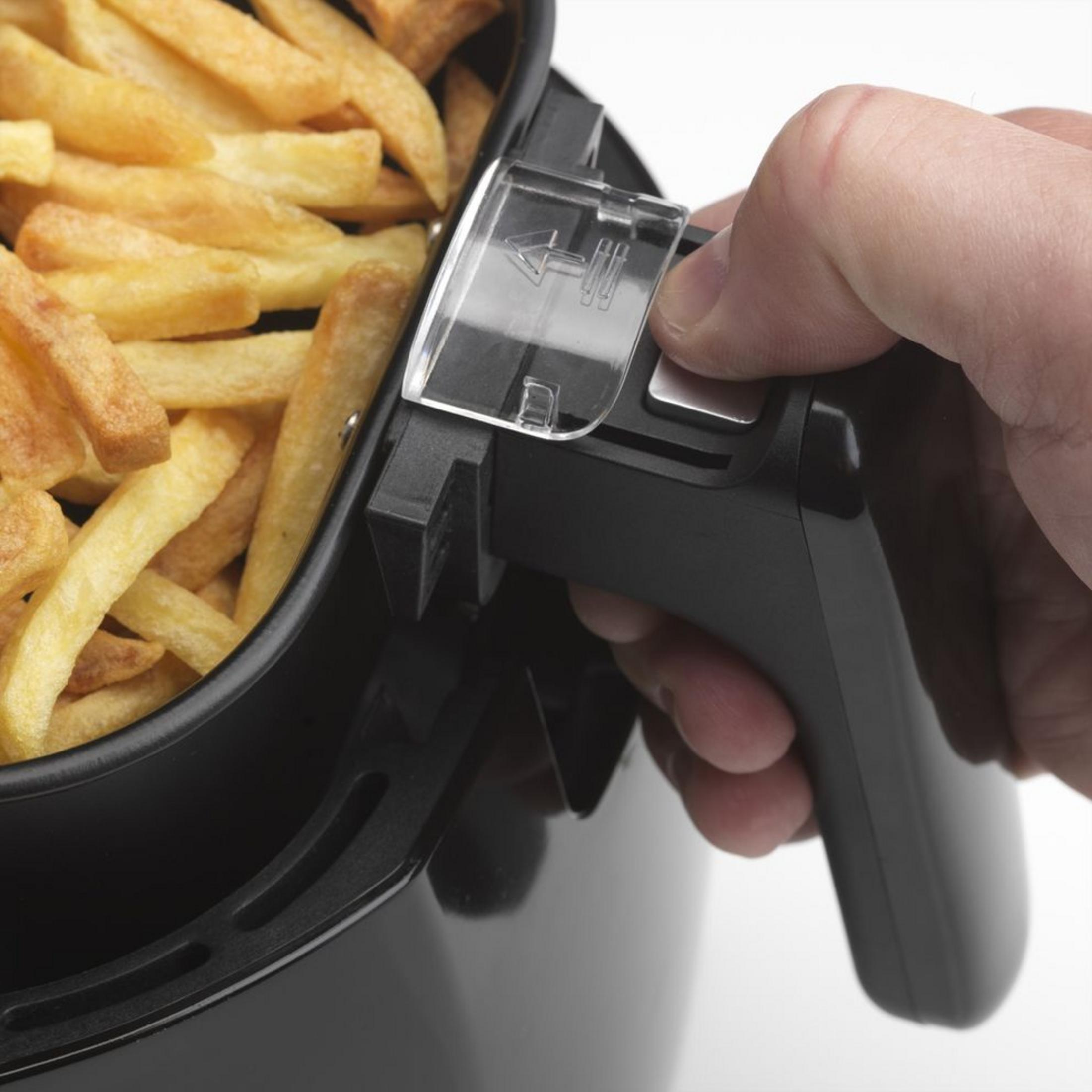 Una mano tiene il manico di un cestello per friggitrice ad aria nero pieno di patatine fritte dorate.