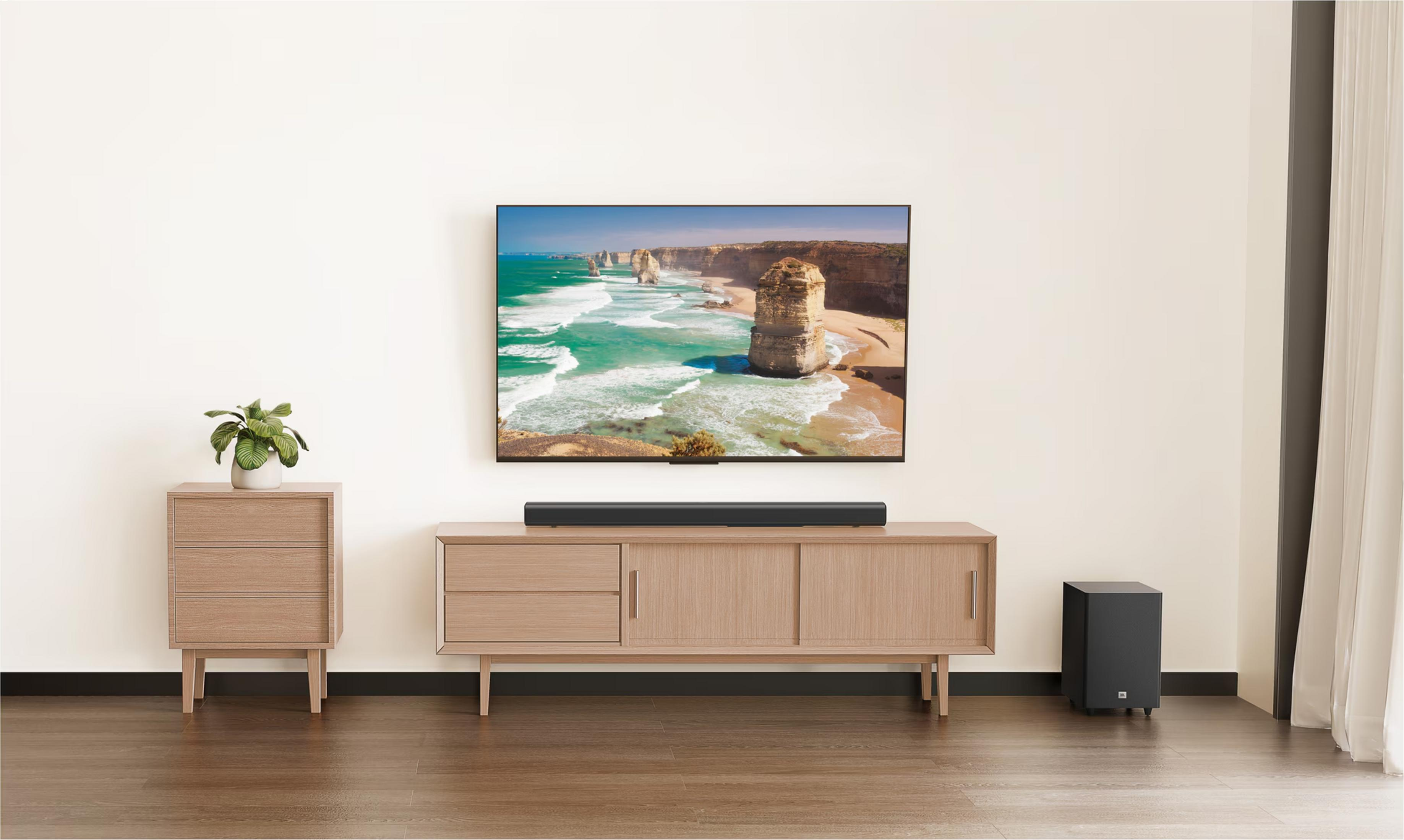 Ein moderner Wohnzimmerschrank mit Fernseher, Soundbar, Subwoofer und Pflanze.