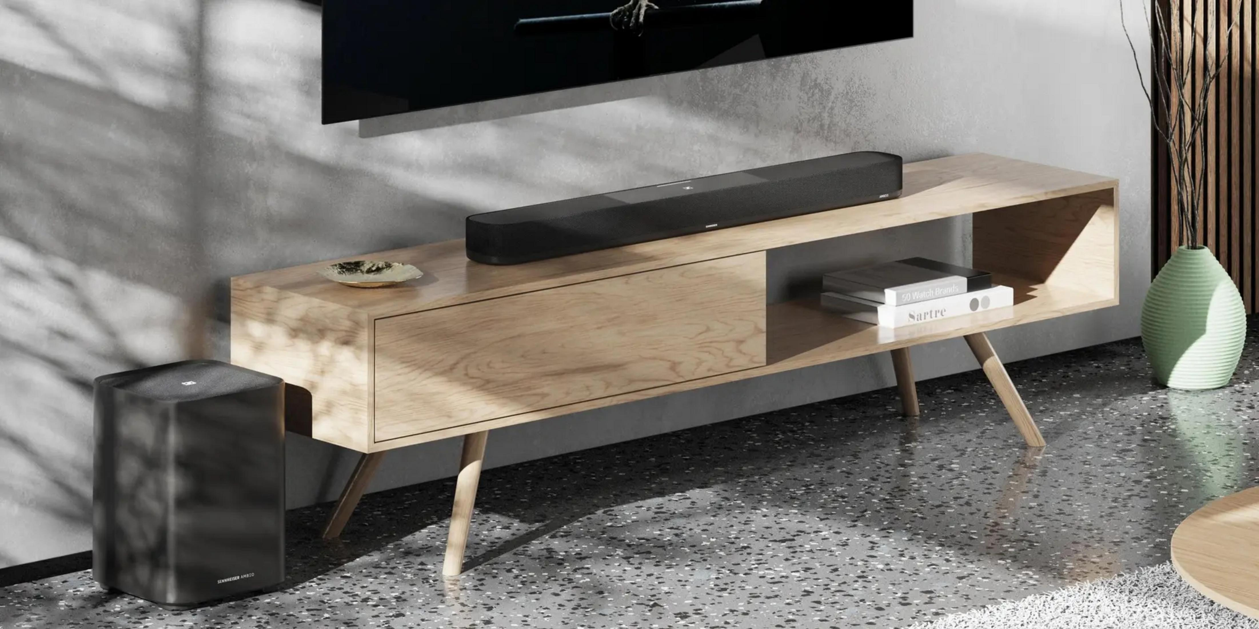 Schwarzer Subwoofer links, Holzkonsole mit Soundbar, Büchern und Schale. Grüner Krug rechts.