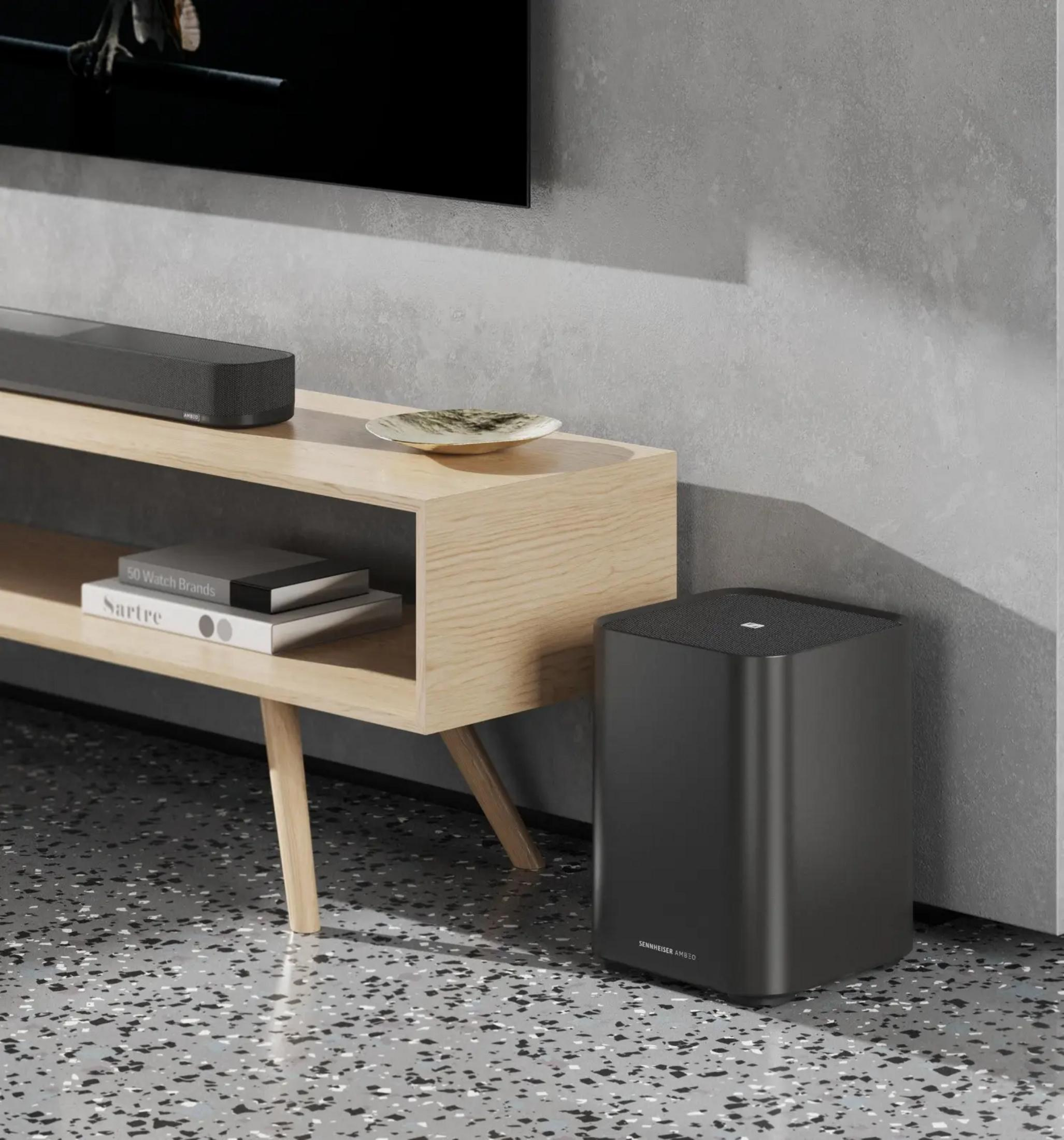 Ein schwarzer Subwoofer steht neben einem Holzfernsehständer mit Büchern und einer Schale.
