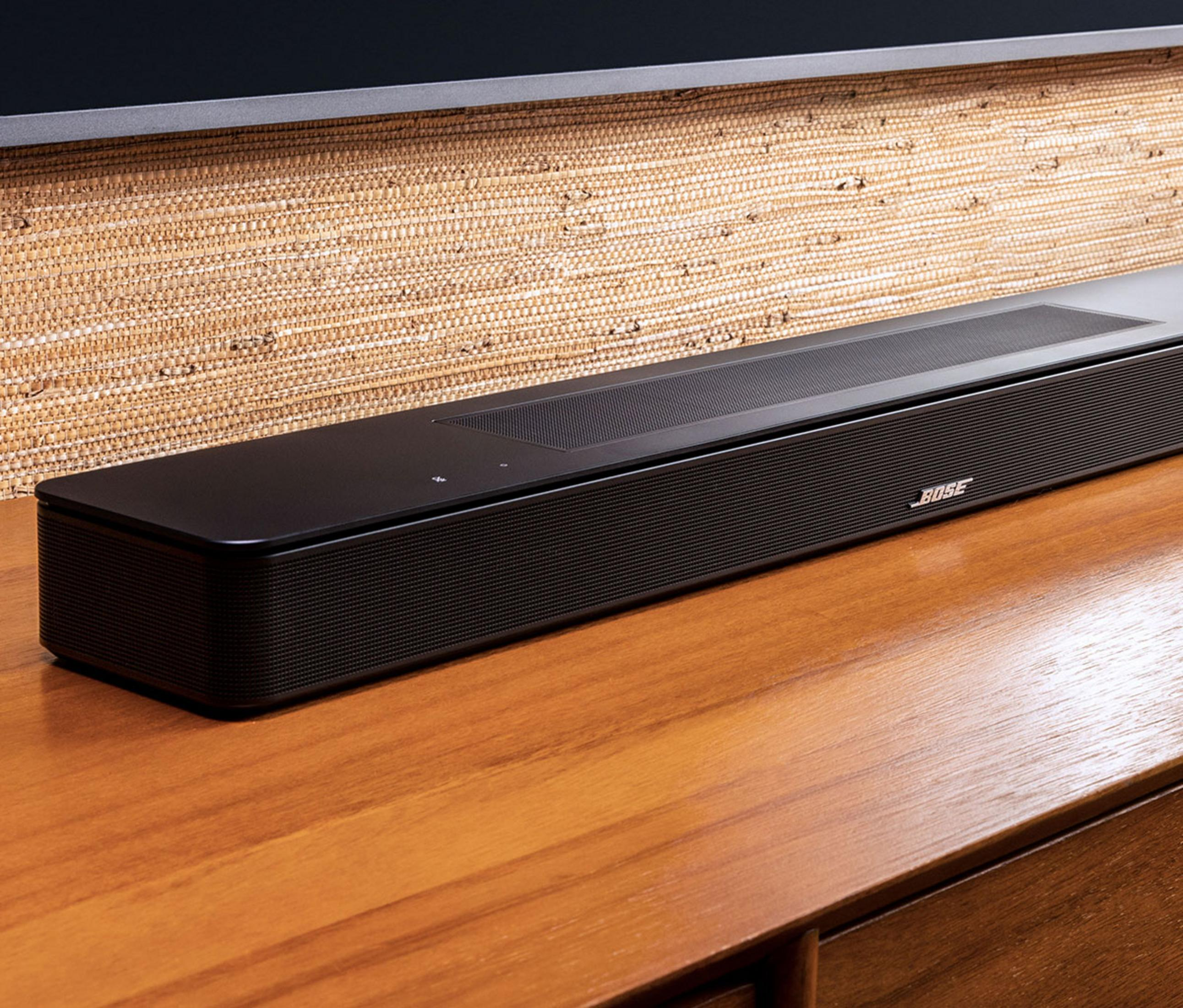 Barra de sonido Bose negra sobre mesa de madera frente a pared texturizada.