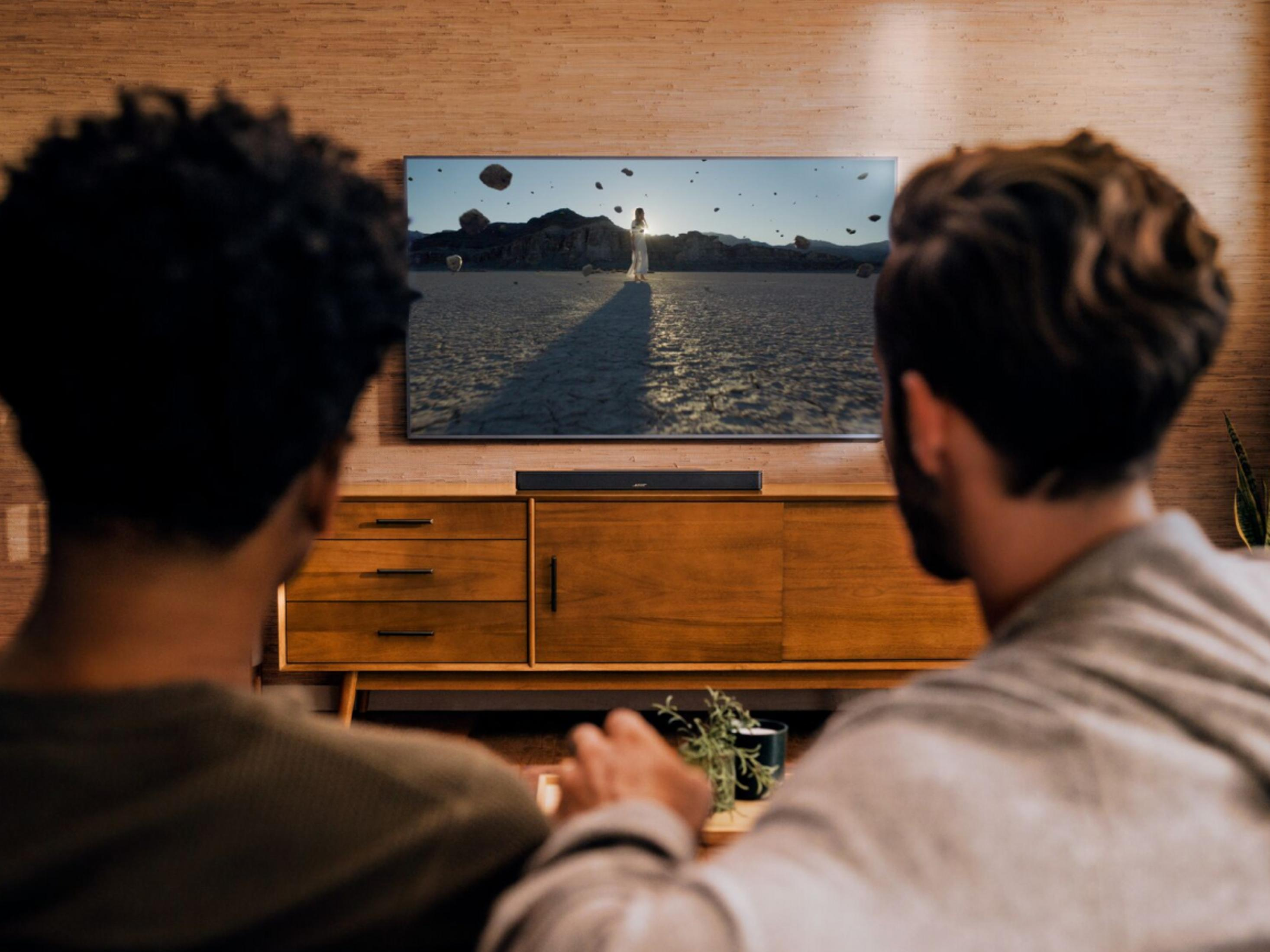 Dos personas ven una película en un televisor sobre un mueble de madera.