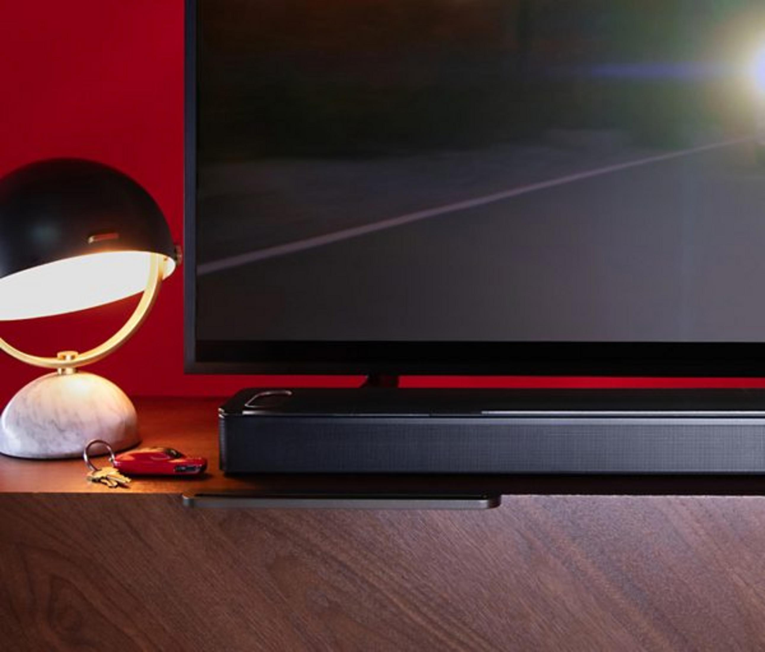 Eine Lampe, ein Autoschlüsselanhänger, ein Fernseher und eine Soundbar auf einem Holztisch.