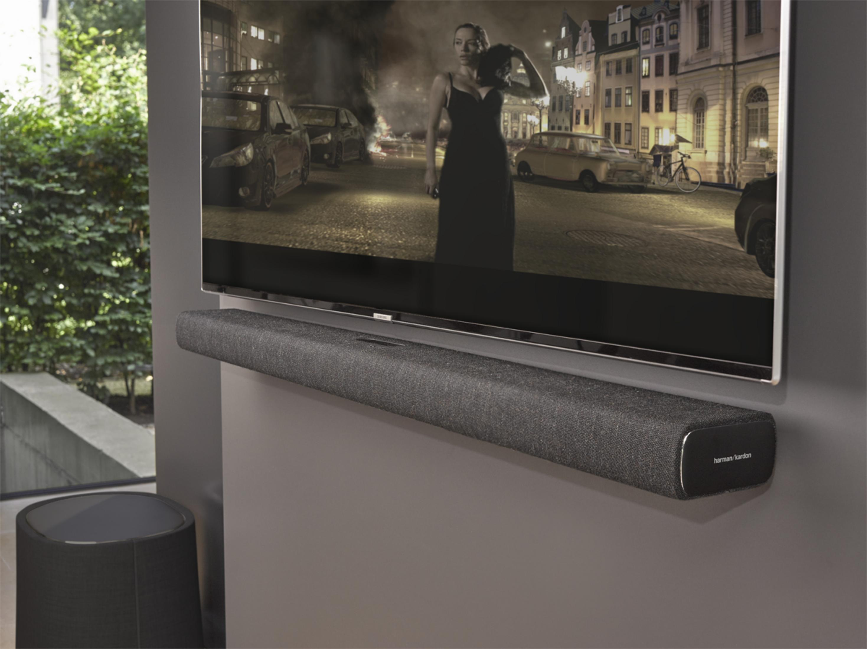 Una TV moderna e una soundbar sono montate su una parete grigia, con un altoparlante scuro accanto.