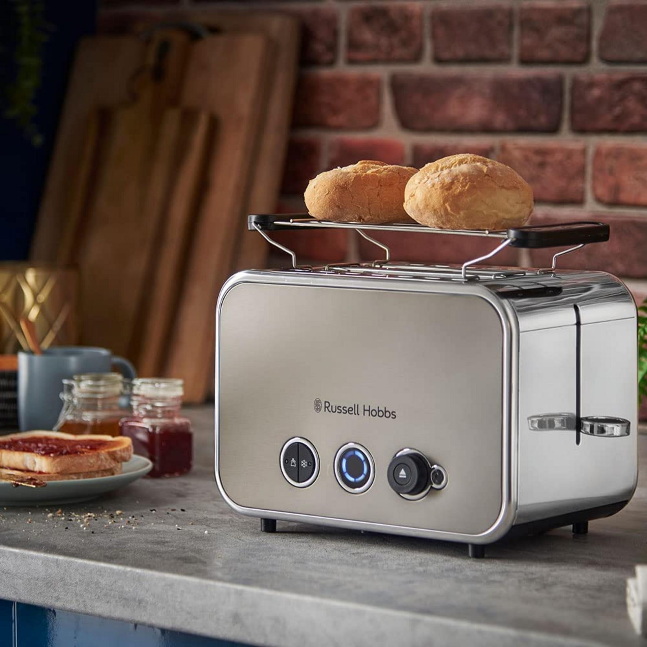 Ein silberner Toaster mit zwei Brötchen auf dem Rost. Daneben Toast mit Marmelade.