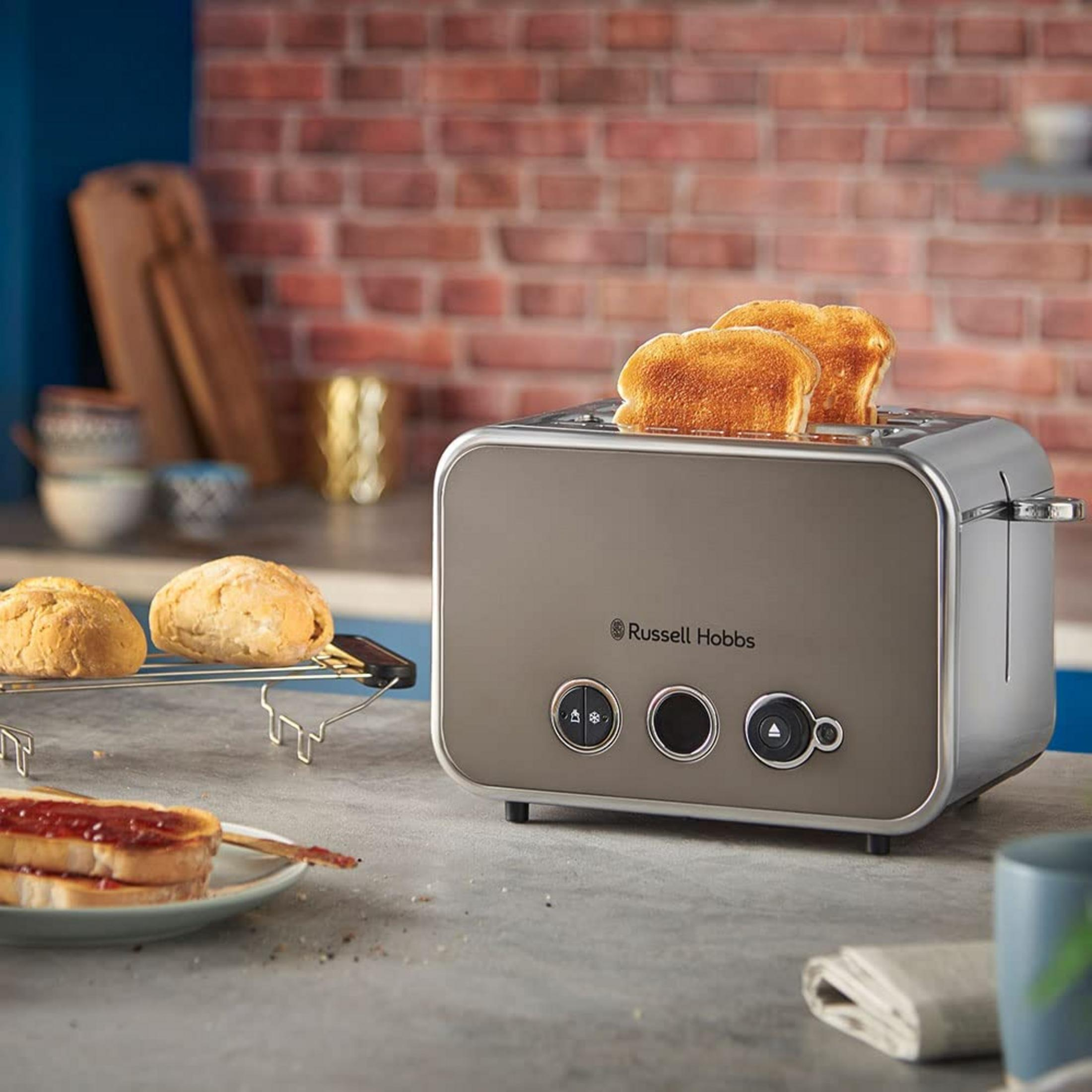 Ein grauer Toaster mit zwei Scheiben Toast und Brötchen daneben.