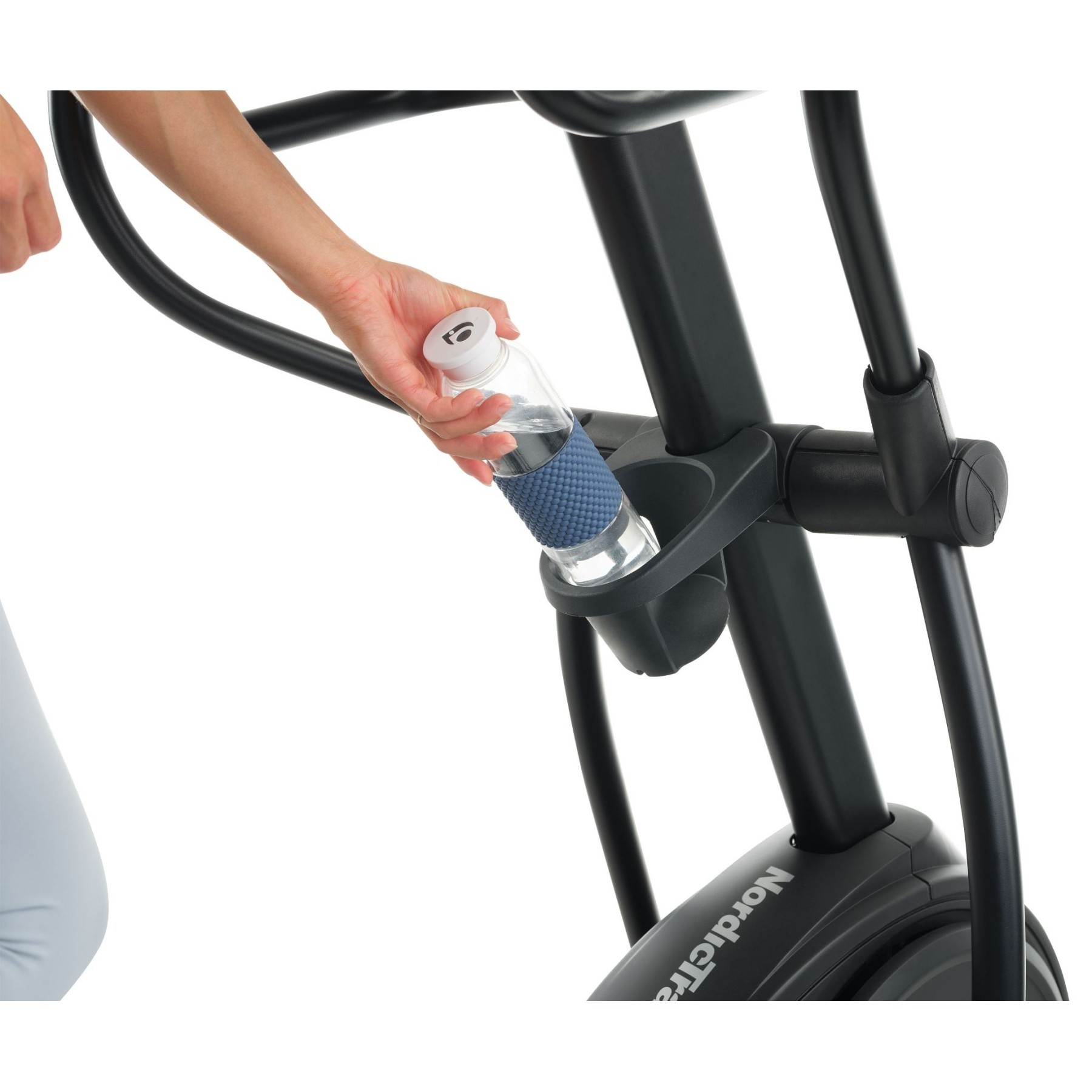 Eine Hand legt eine Wasserflasche in den Halter eines schwarzen Trainingsgeräts.