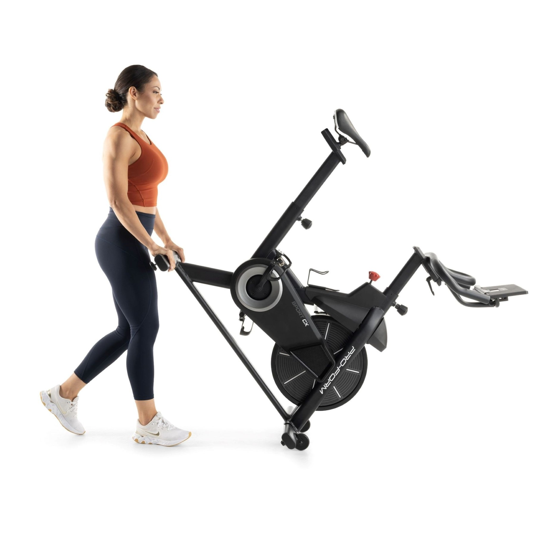 Kobieta w stroju sportowym pcha czarny rower stacjonarny na białym tle.