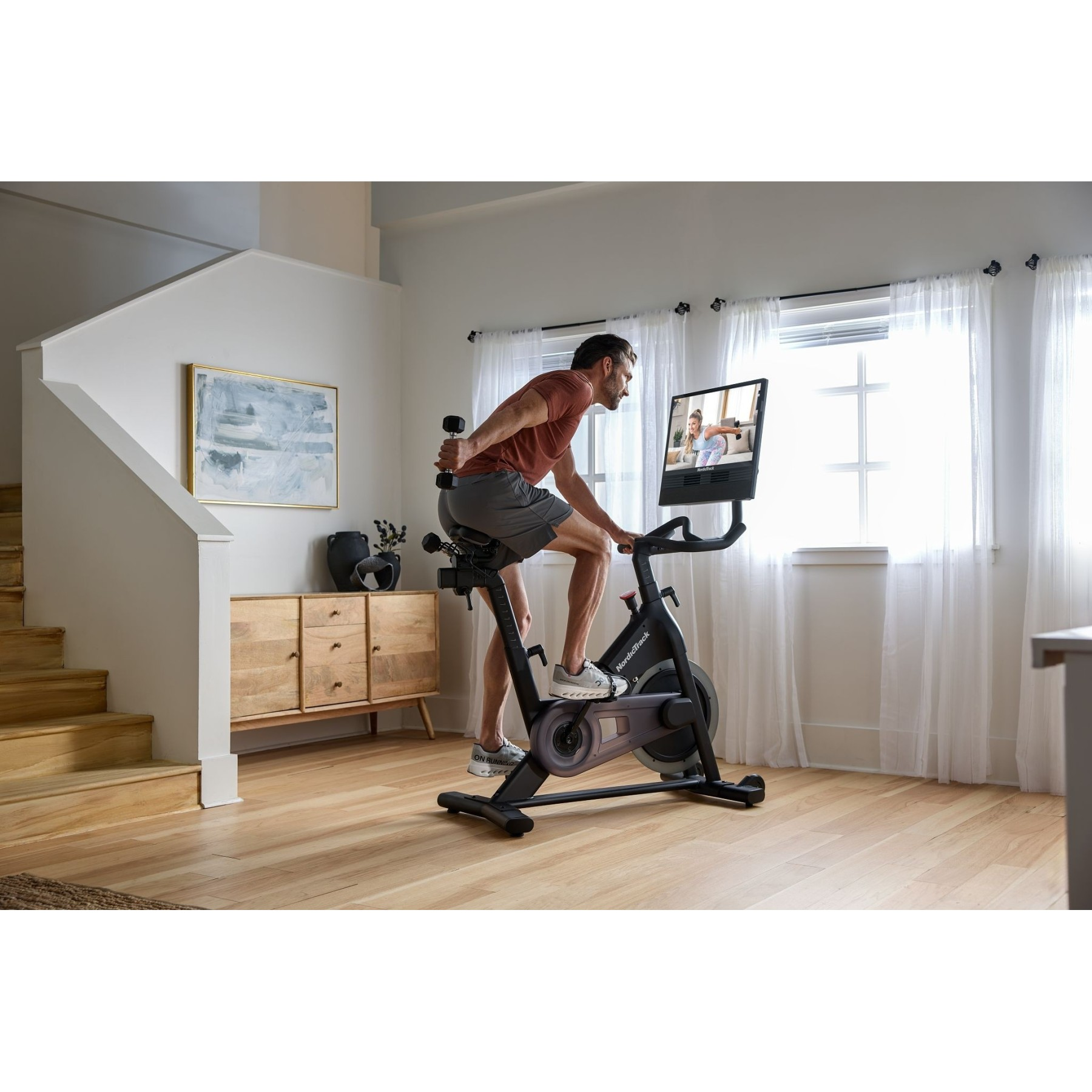 Ein Mann trainiert auf einem Heimtrainer vor einem Bildschirm, der eine Trainerin zeigt.