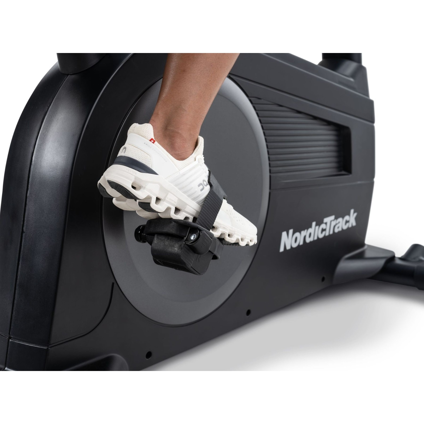 Ein Fuß in einem weißen Schuh tritt auf ein schwarzes Pedal eines NordicTrack-Heimtrainers.