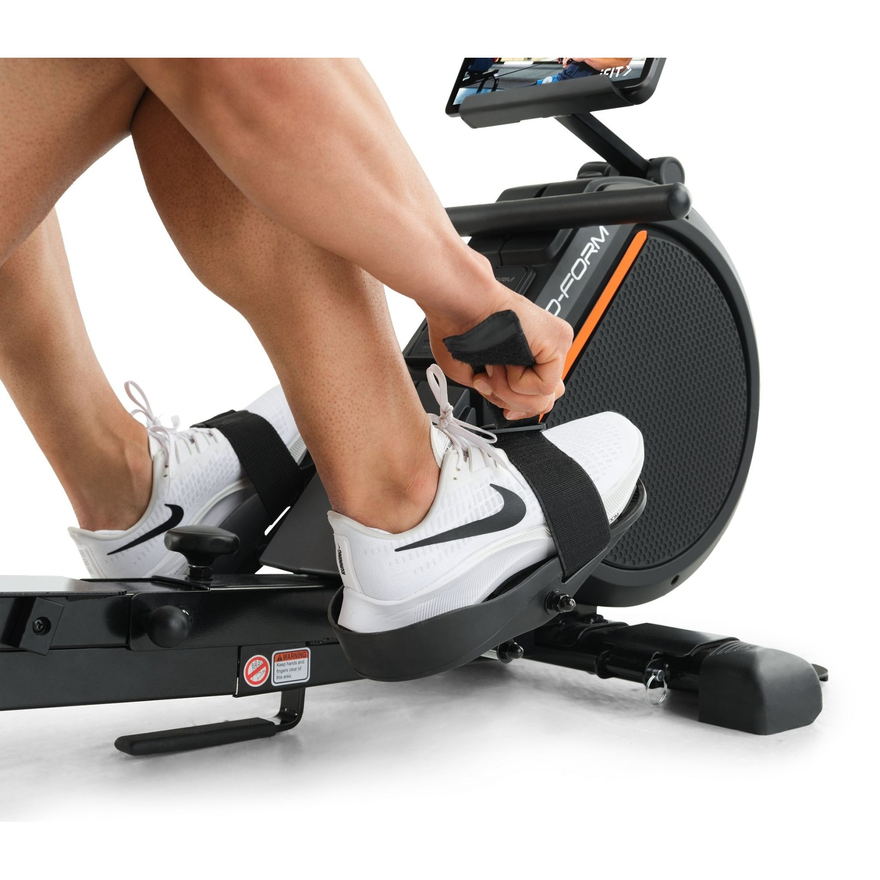 Eine Person rudert auf einem Heimtrainer mit weißen Turnschuhen und schwarzem Griff.