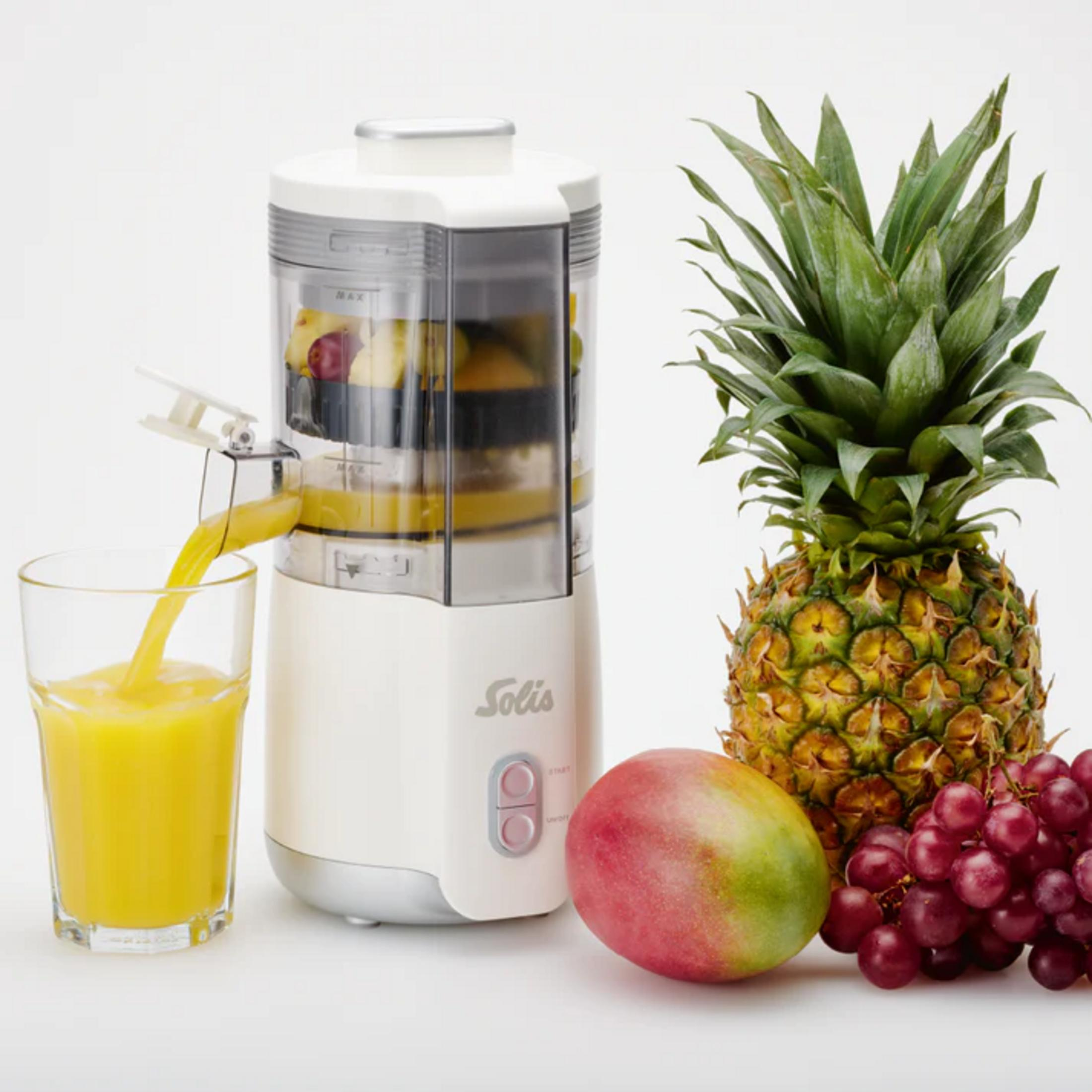 Un estrattore versa succo in un bicchiere. Ananas, mango e uva nelle vicinanze.