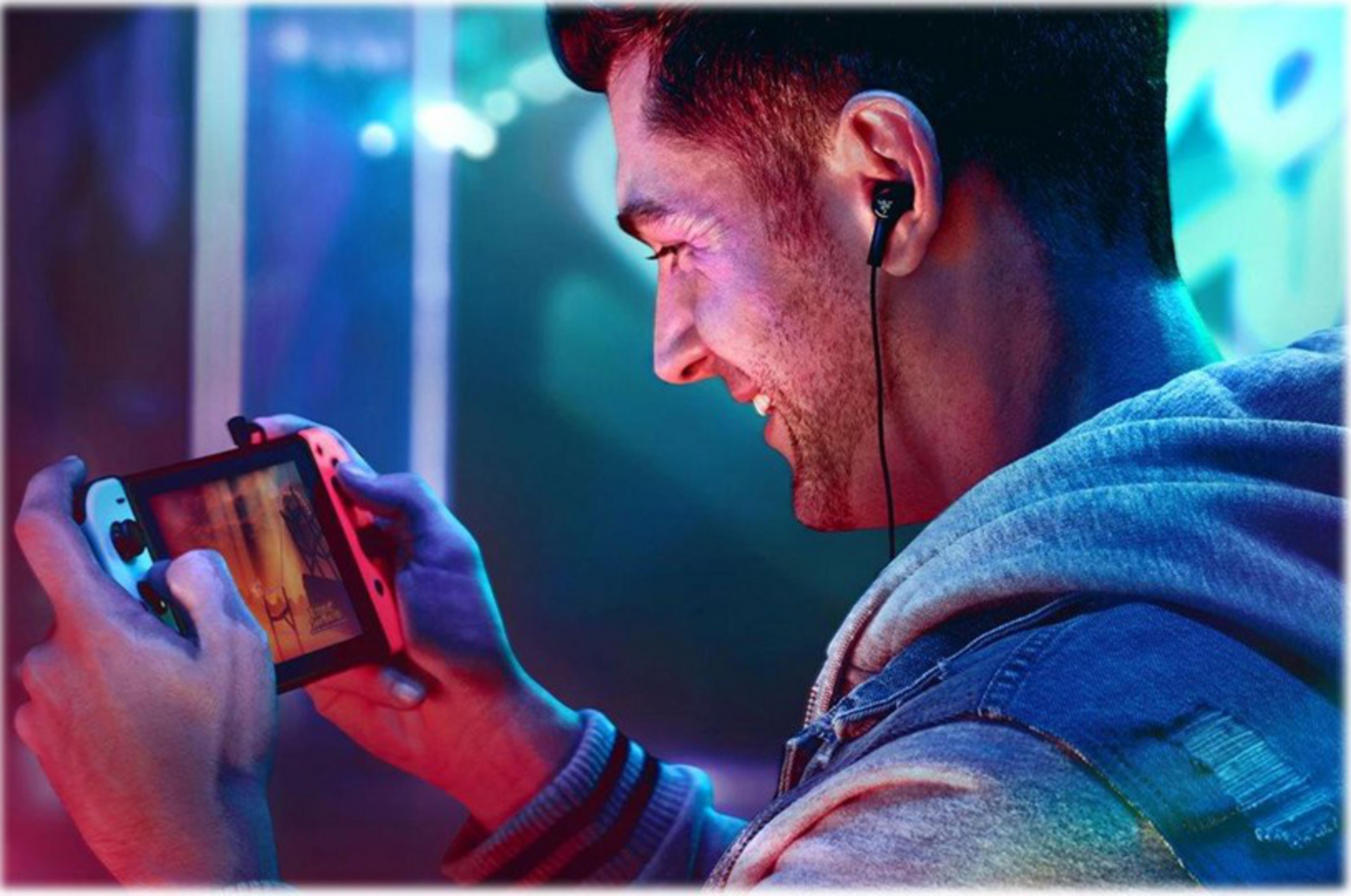 Homme jouant à un jeu vidéo sur Nintendo Switch avec écouteurs. Éclairage bleu et rouge.