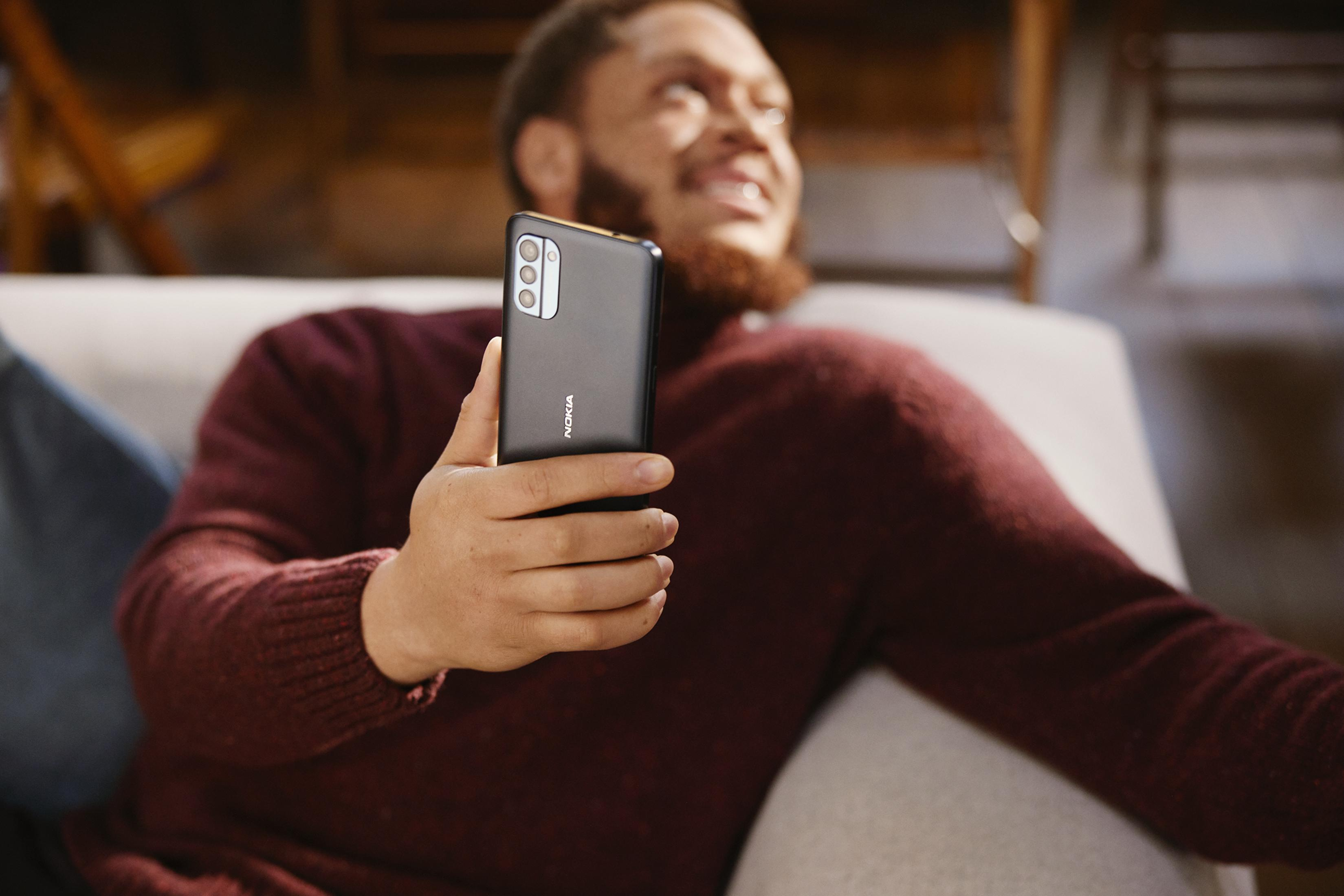 Mężczyzna trzyma telefon Nokia z trzema aparatami, siedzi na kanapie.