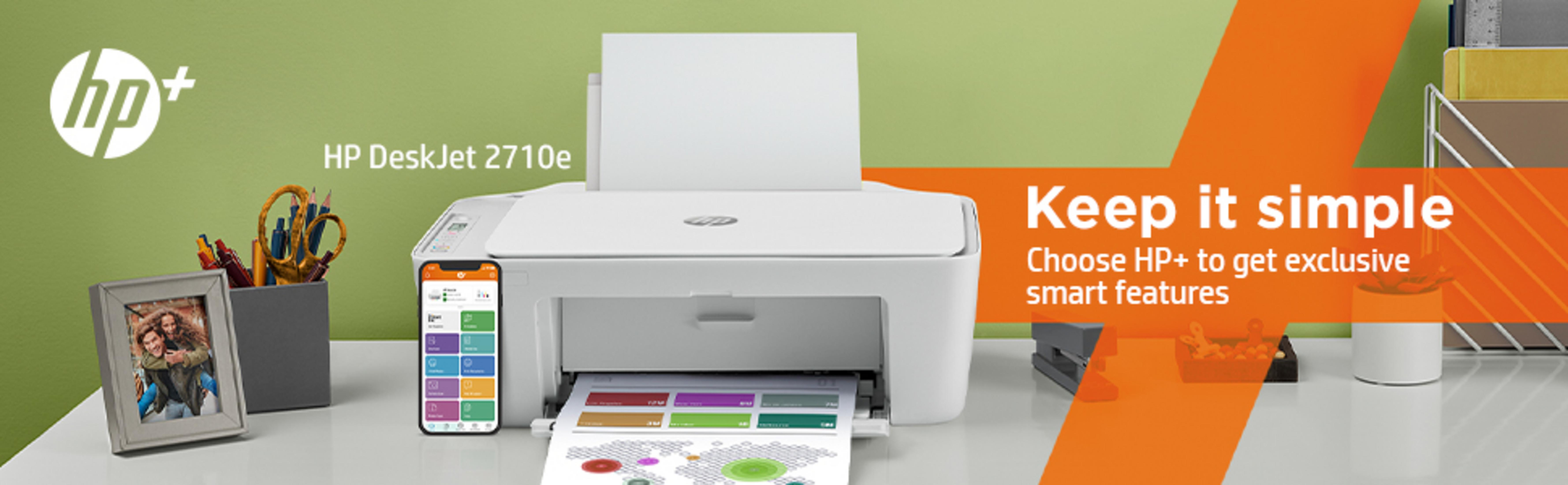 Una impresora HP DeskJet 2710e con smartphone, foto y material de oficina en un escritorio.