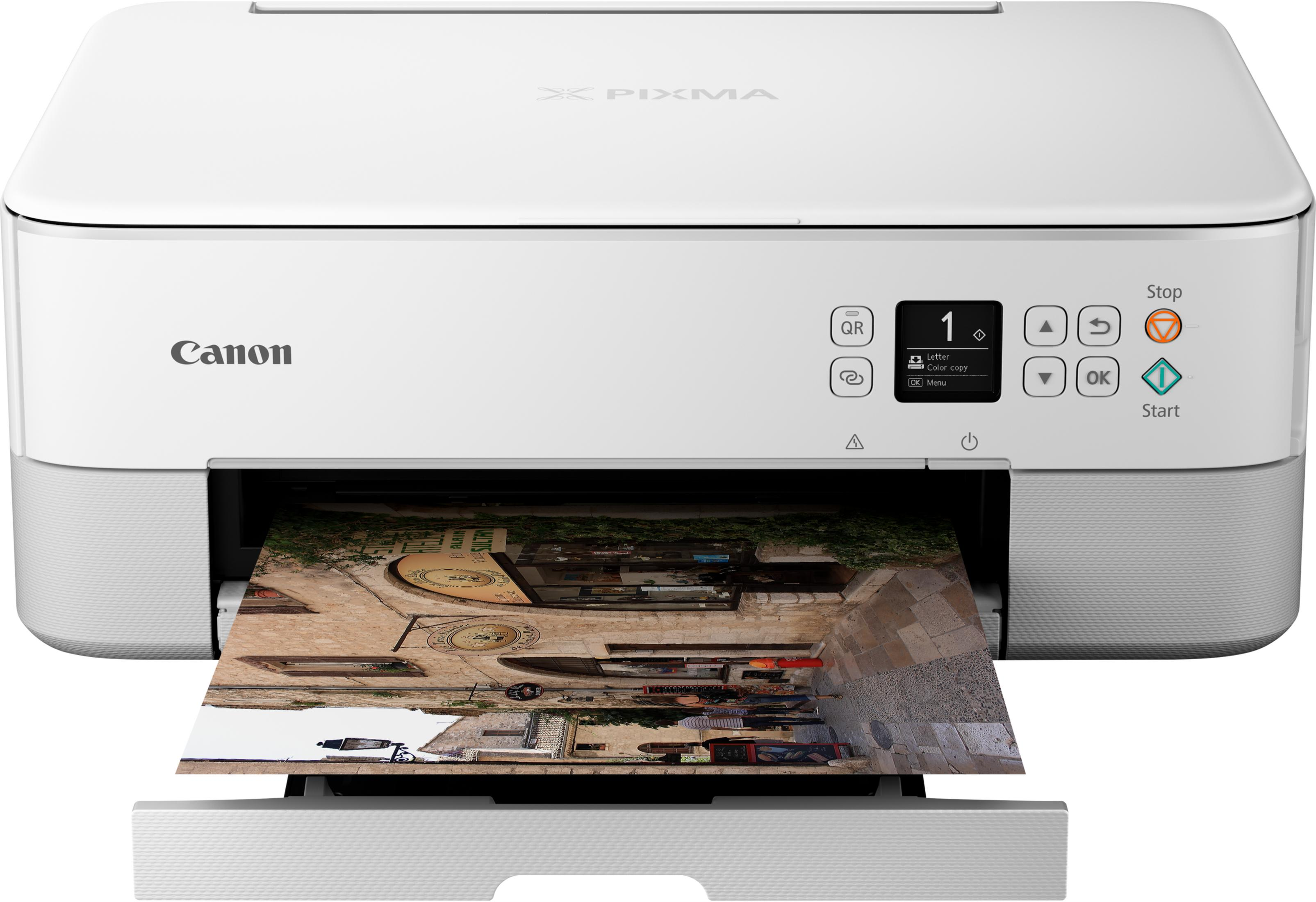 Biała drukarka Canon Pixma drukuje obraz uliczki ze sklepami.