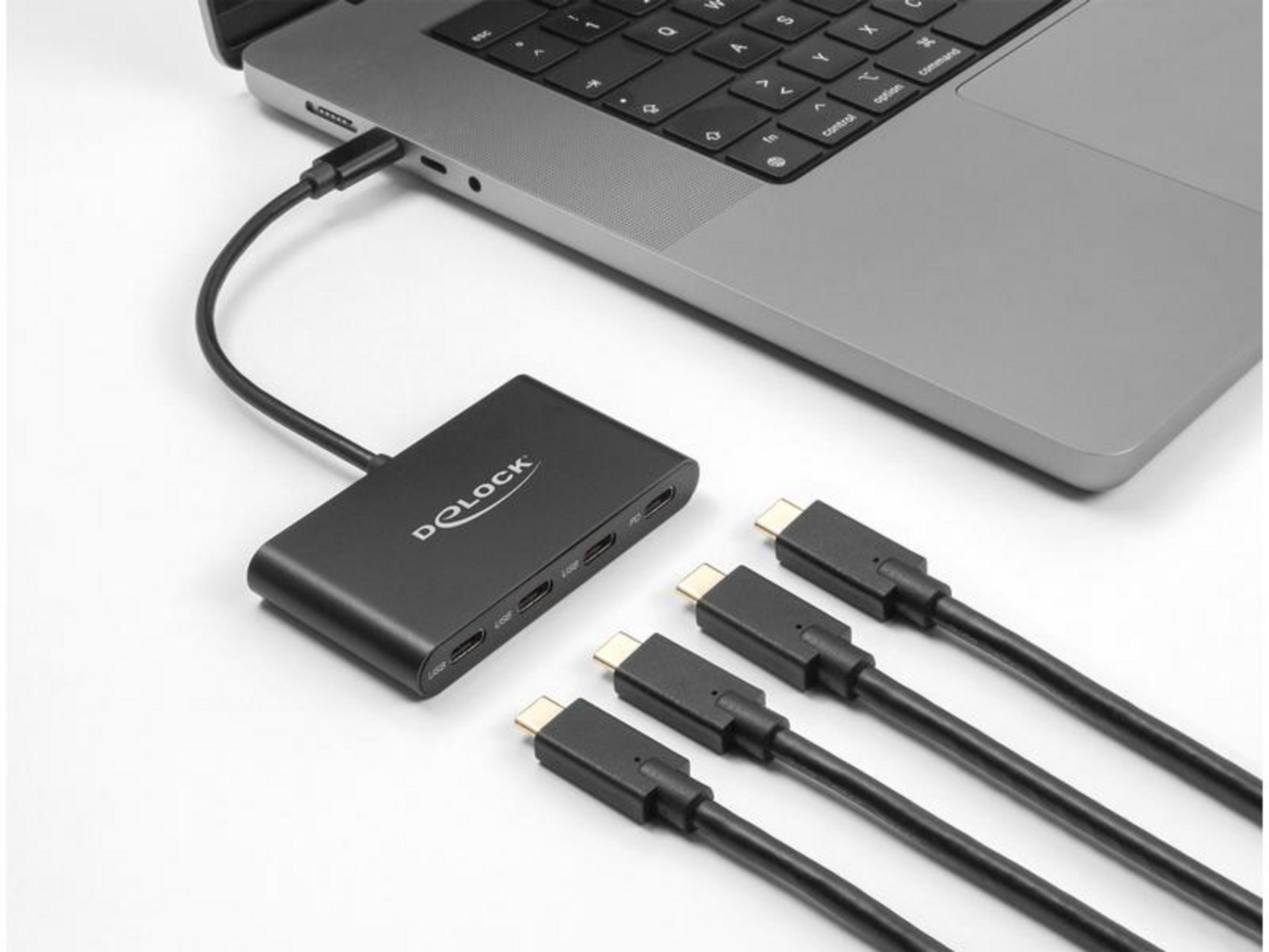 Ein schwarzer USB-C-Hub ist an einen Laptop angeschlossen. Drei weitere USB-C-Kabel liegen daneben.
