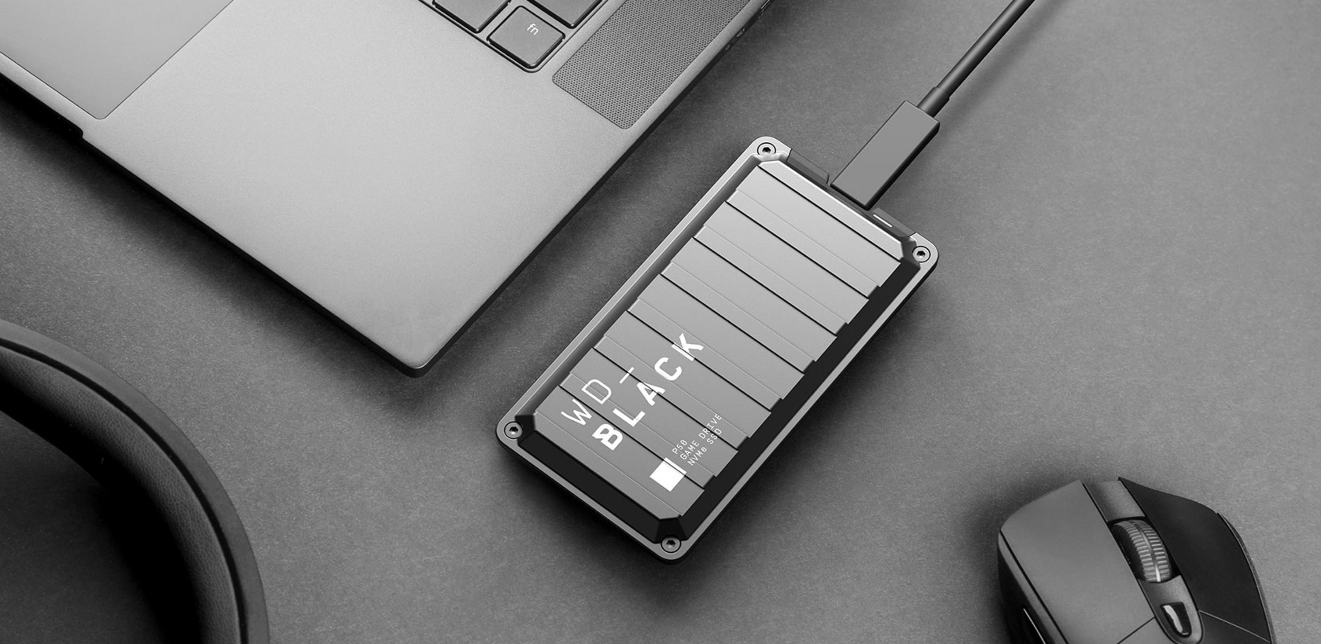 Ein Laptop, eine externe Festplatte und eine Maus liegen auf einem dunklen Schreibtisch.