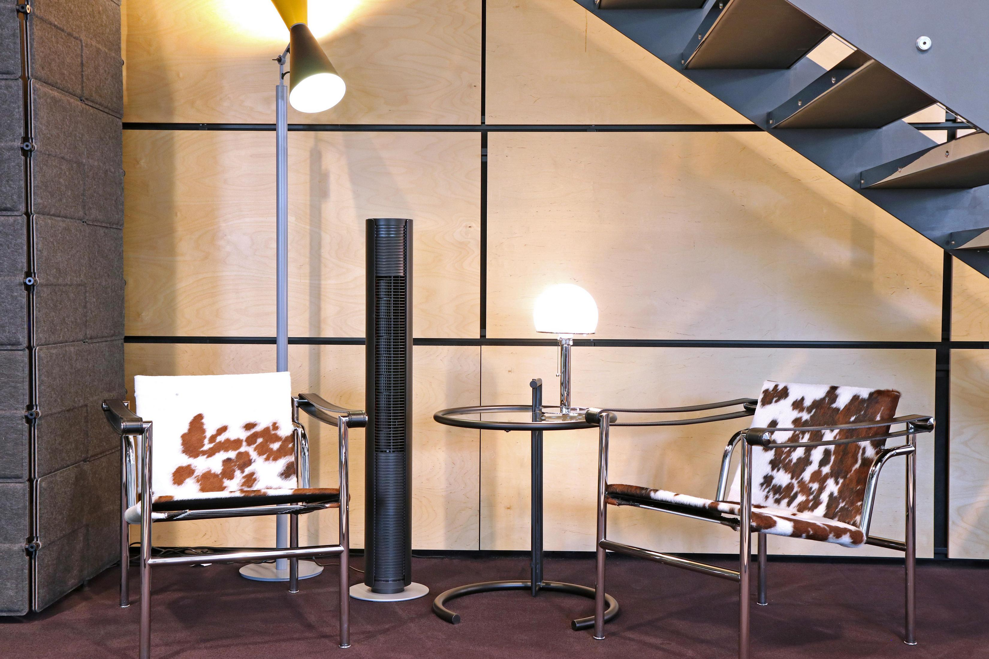 Deux chaises en peau de vache flanquent un ventilateur tour et une table sous un escalier.