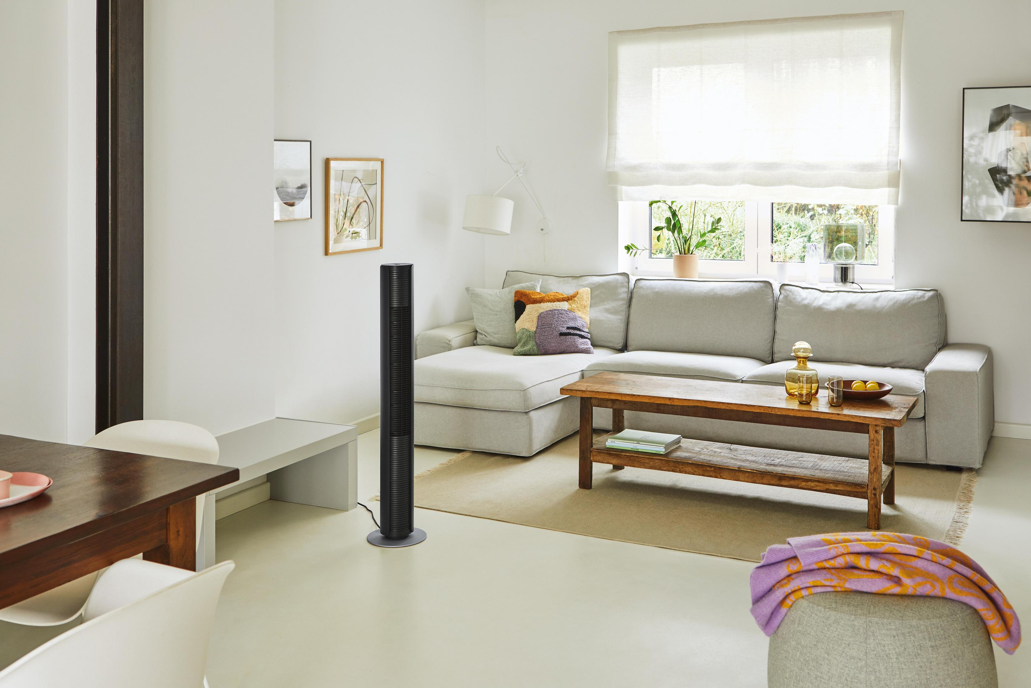 Un espace de vie lumineux avec canapé, table basse, ventilateur et coin repas.