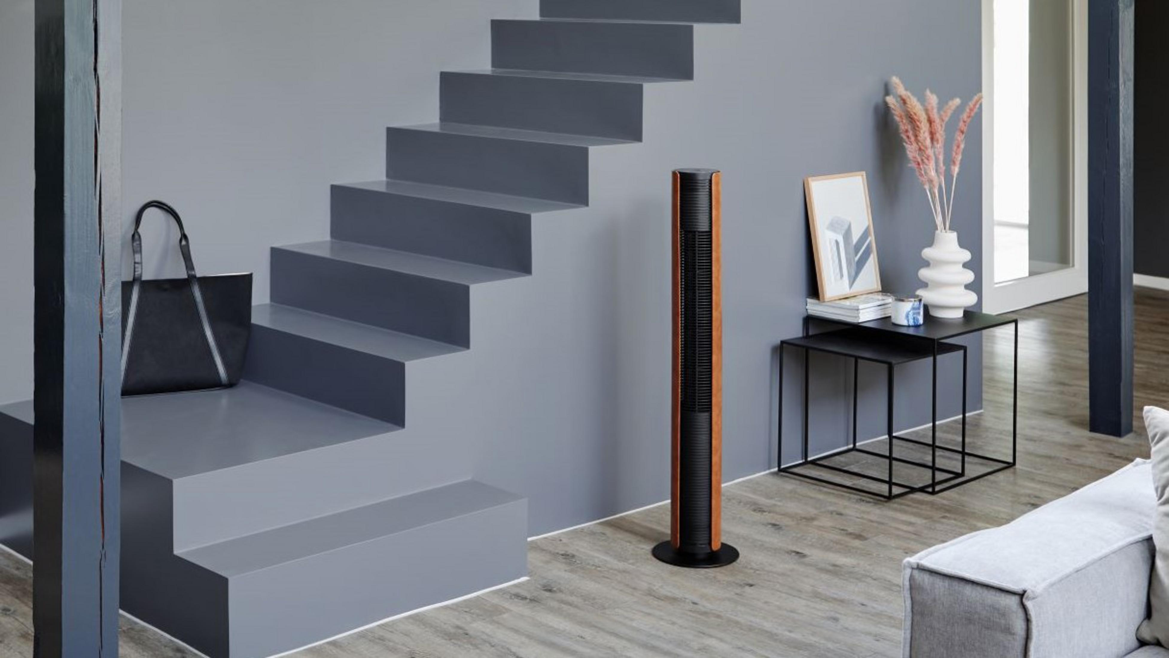Ein moderner Wohnraum mit grauen Treppen, einem Turmventilator und Deko.