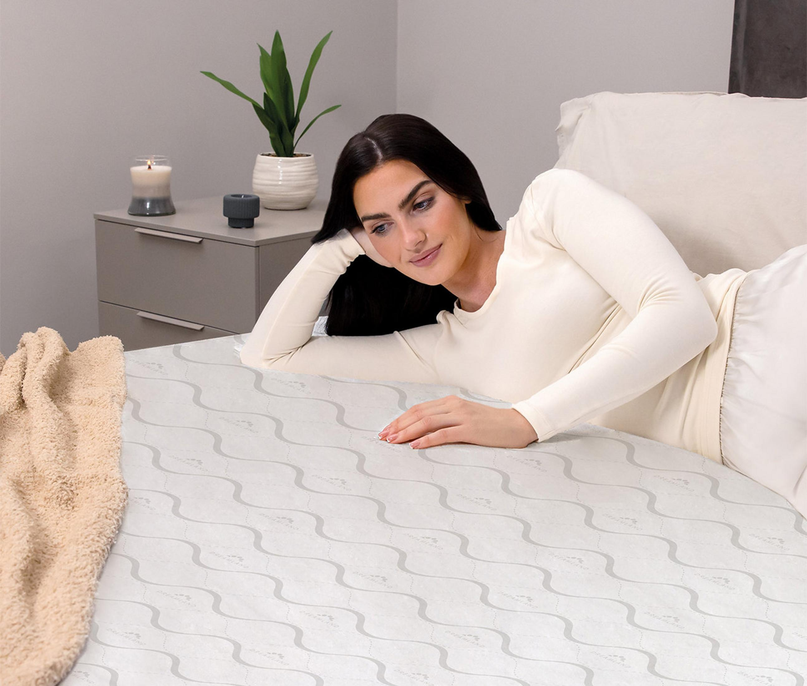 A woman lies on a bed with a blanket and a nightstand in the background.