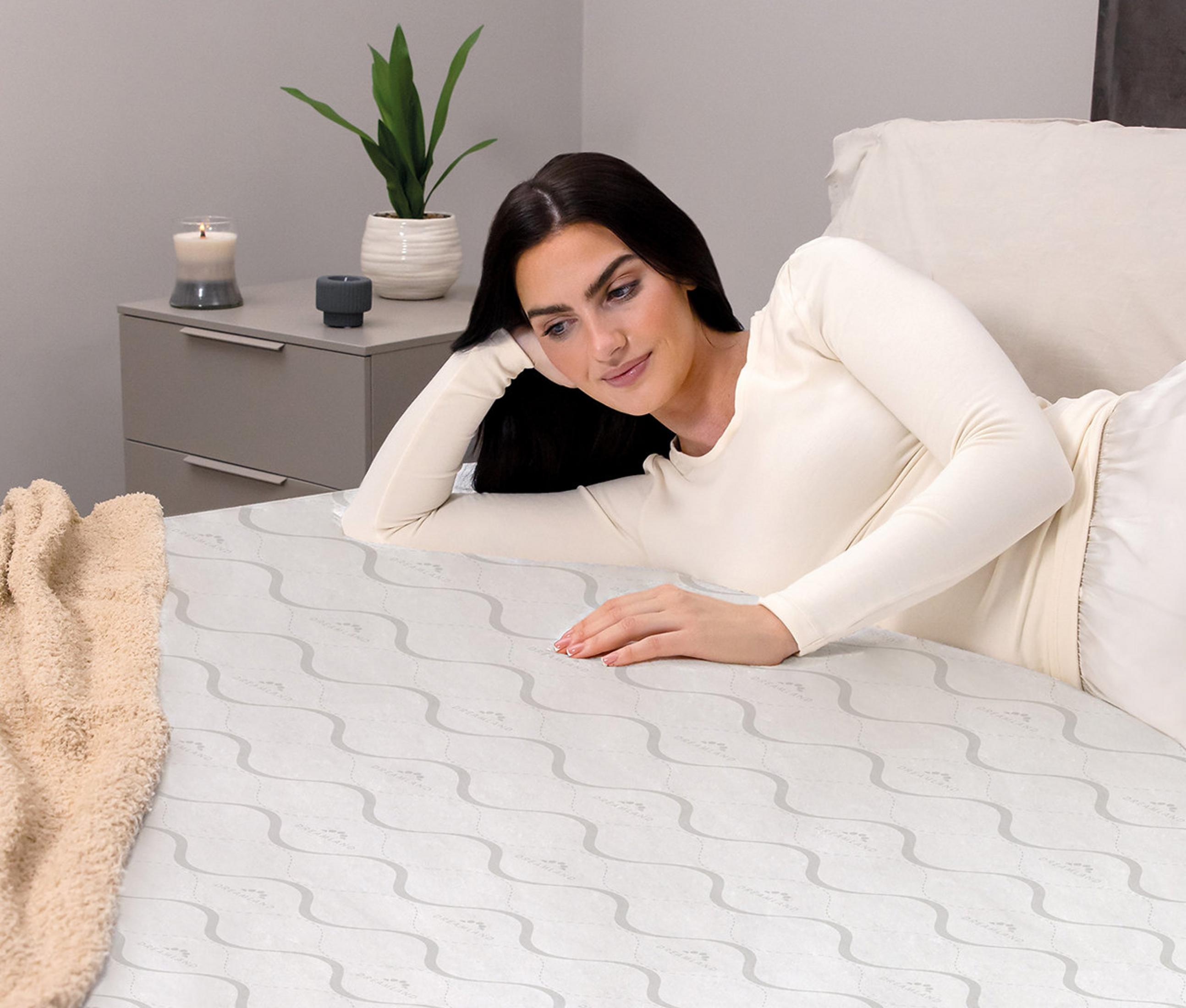 A woman lies on a bed with a wave pattern. A blanket is on the left.