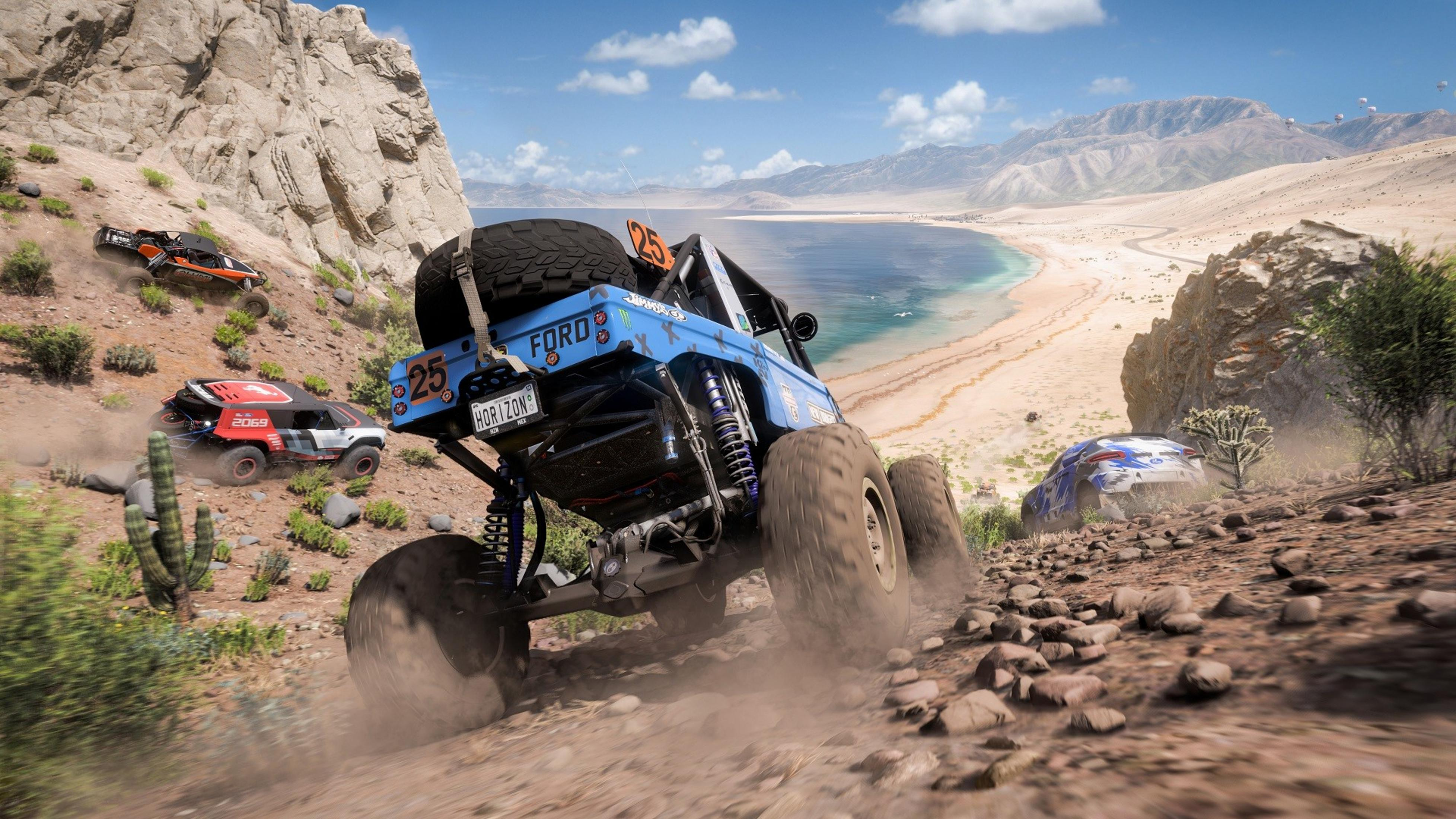Offroad-Rennwagen fahren auf felsigem Hang mit blauem Himmel und Ozean im Hintergrund.