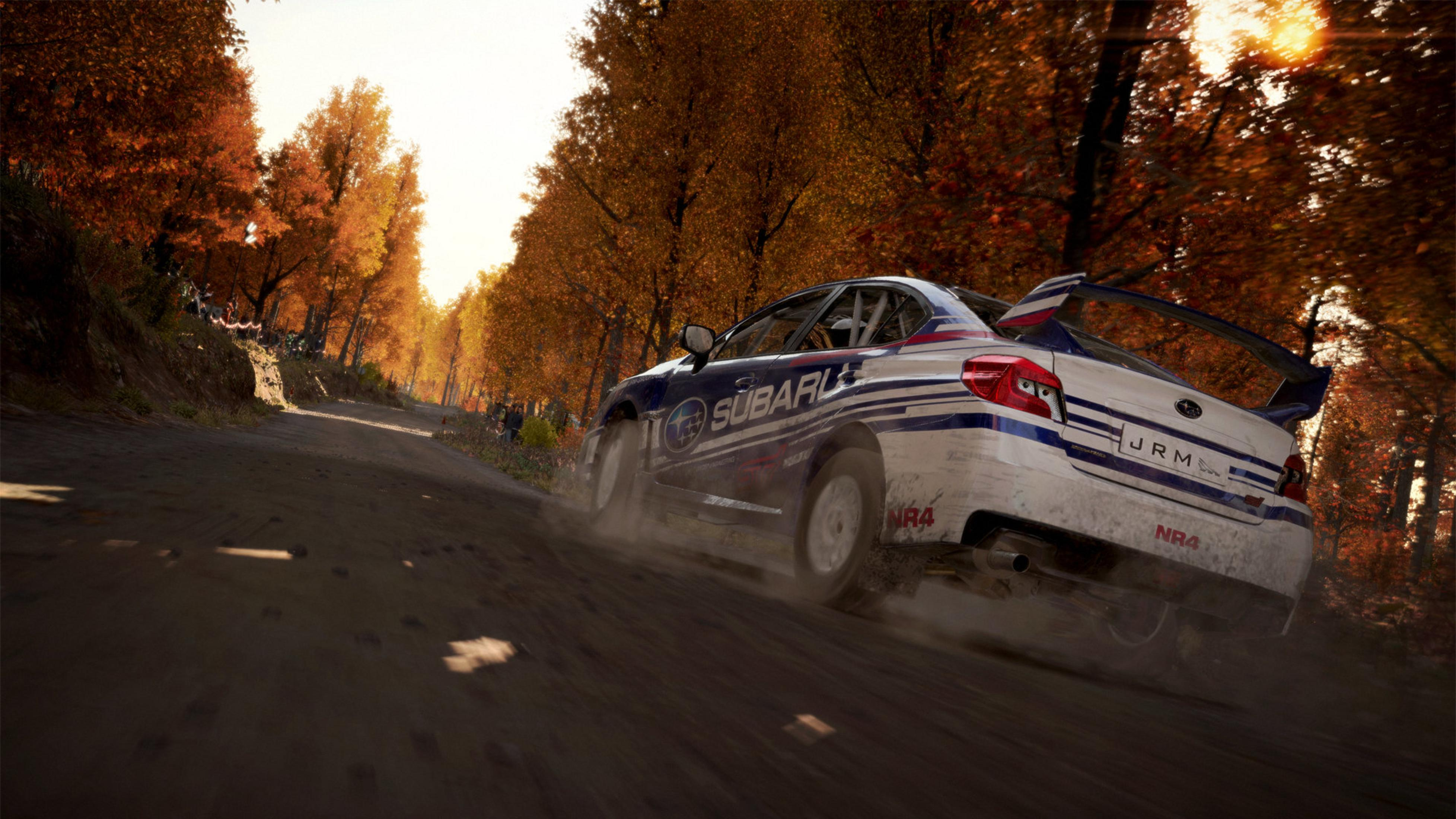 Un'auto da rally Subaru bianca con strisce blu guida su una strada sterrata in autunno.