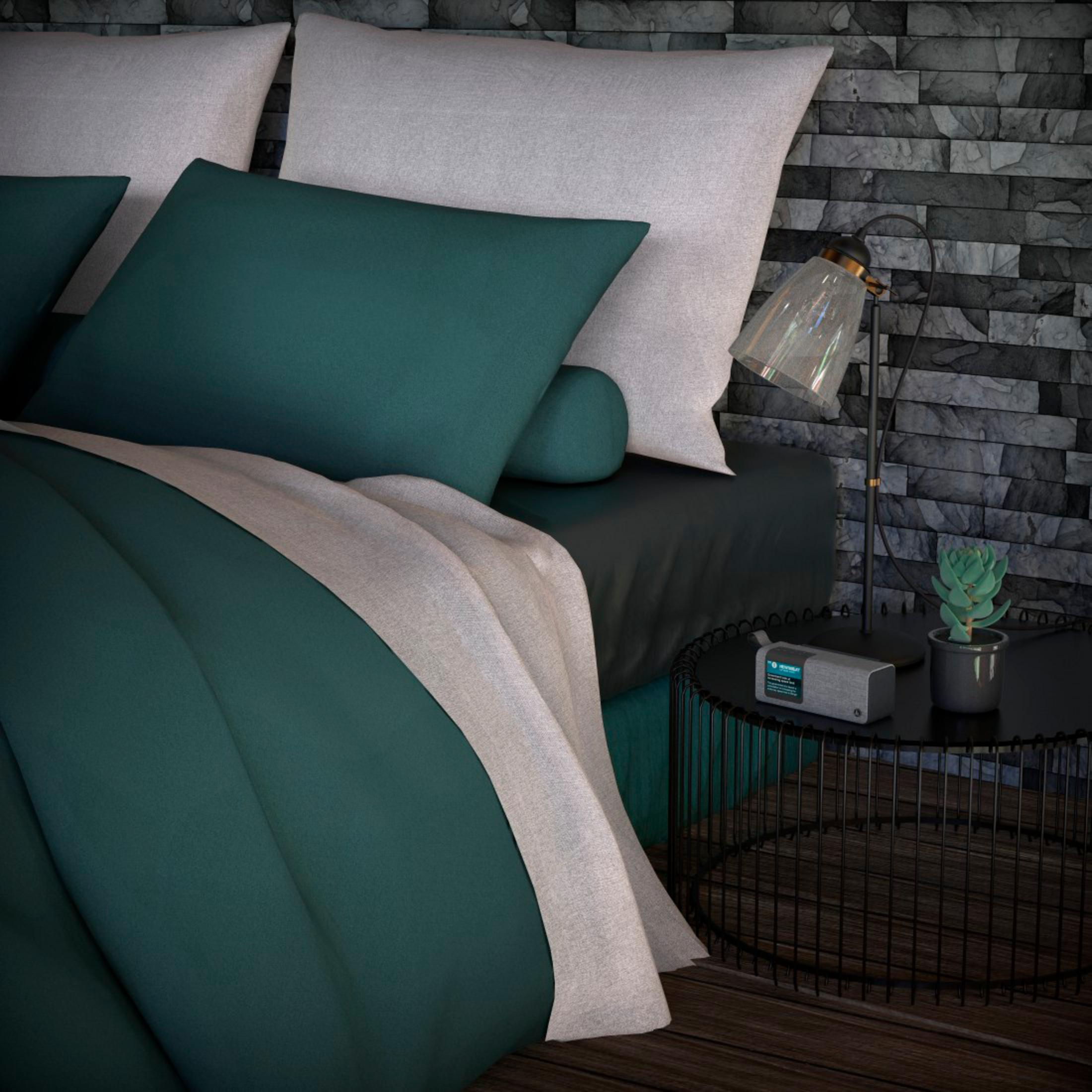 Un letto con biancheria da letto verde scuro, cuscini grigi e carta da parati effetto pietra.