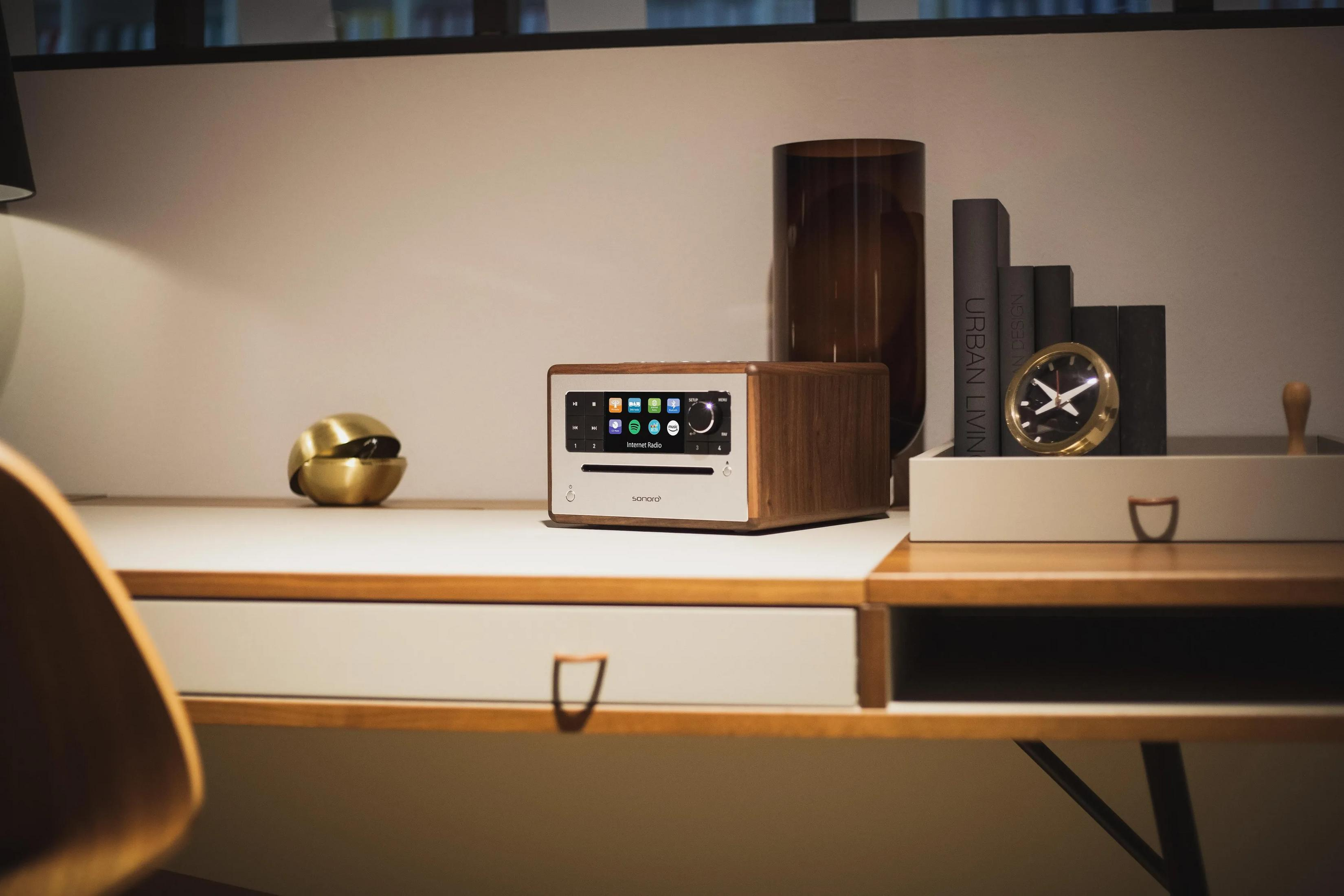 Een modern bureau met radio van hout, messing bol, vaas, boeken en dienblad met klok.