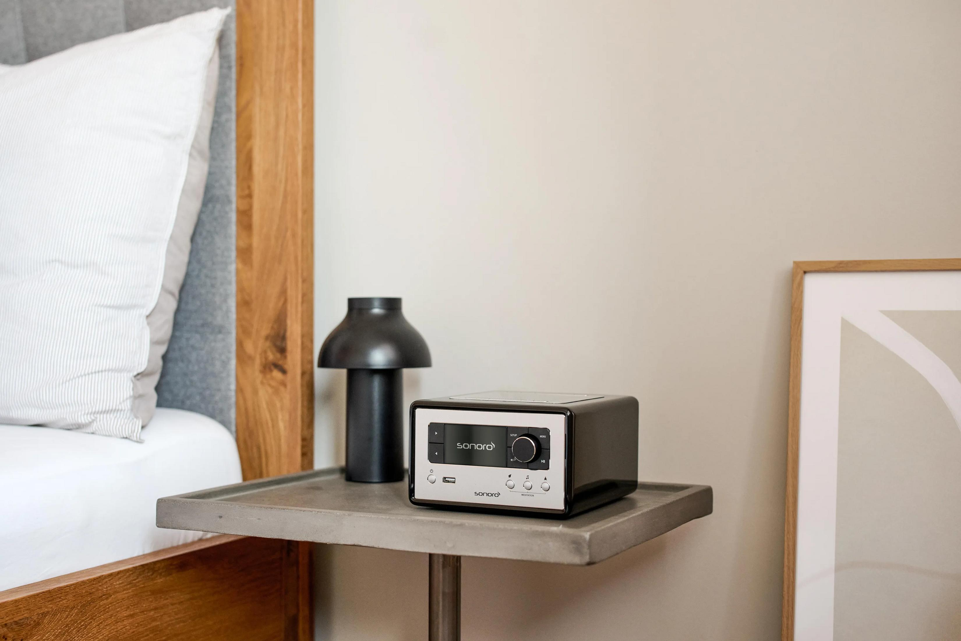 A bedside table with a radio, a lamp and a bed in the background.