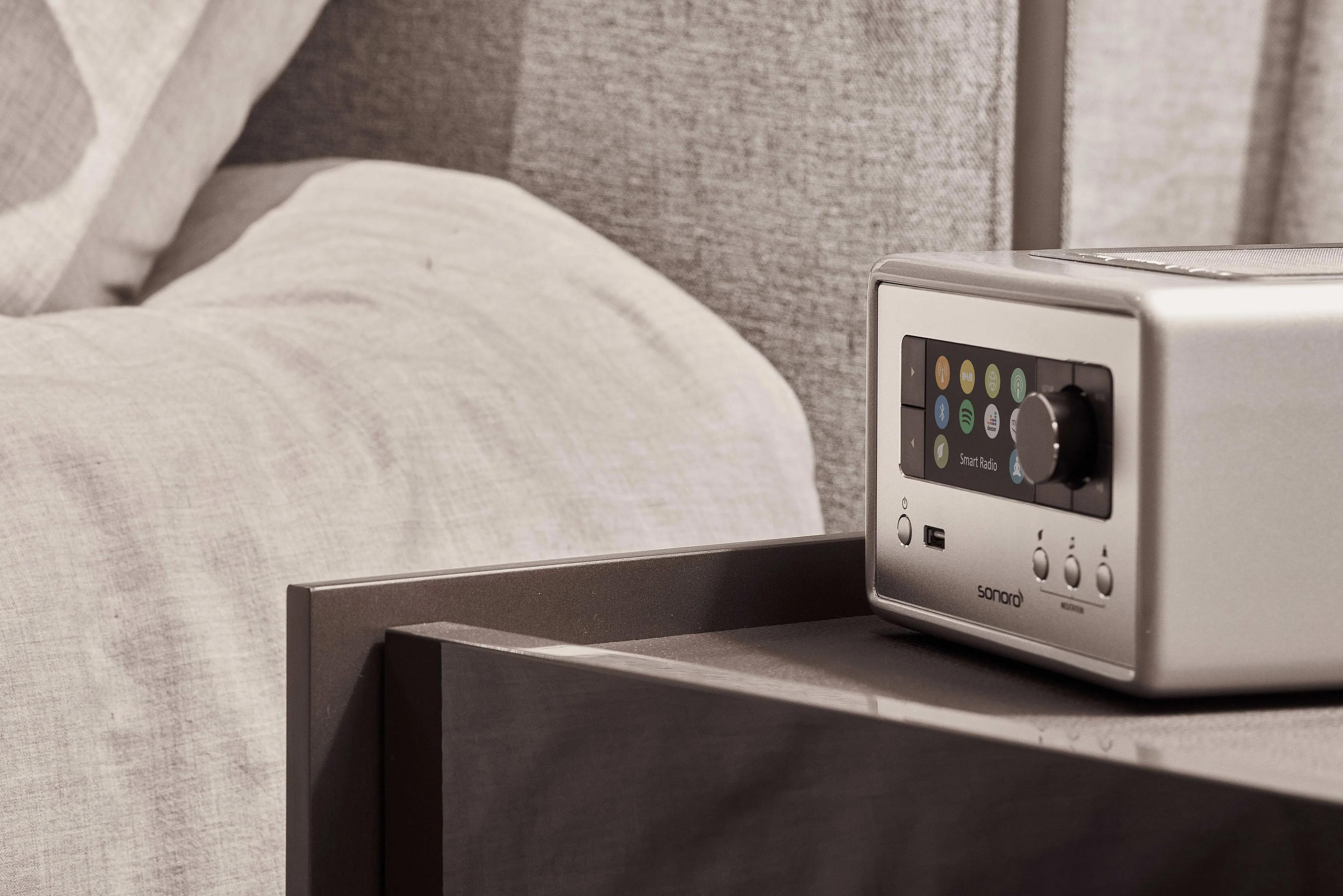A silver radio sits on a nightstand next to a bed with gray linens.