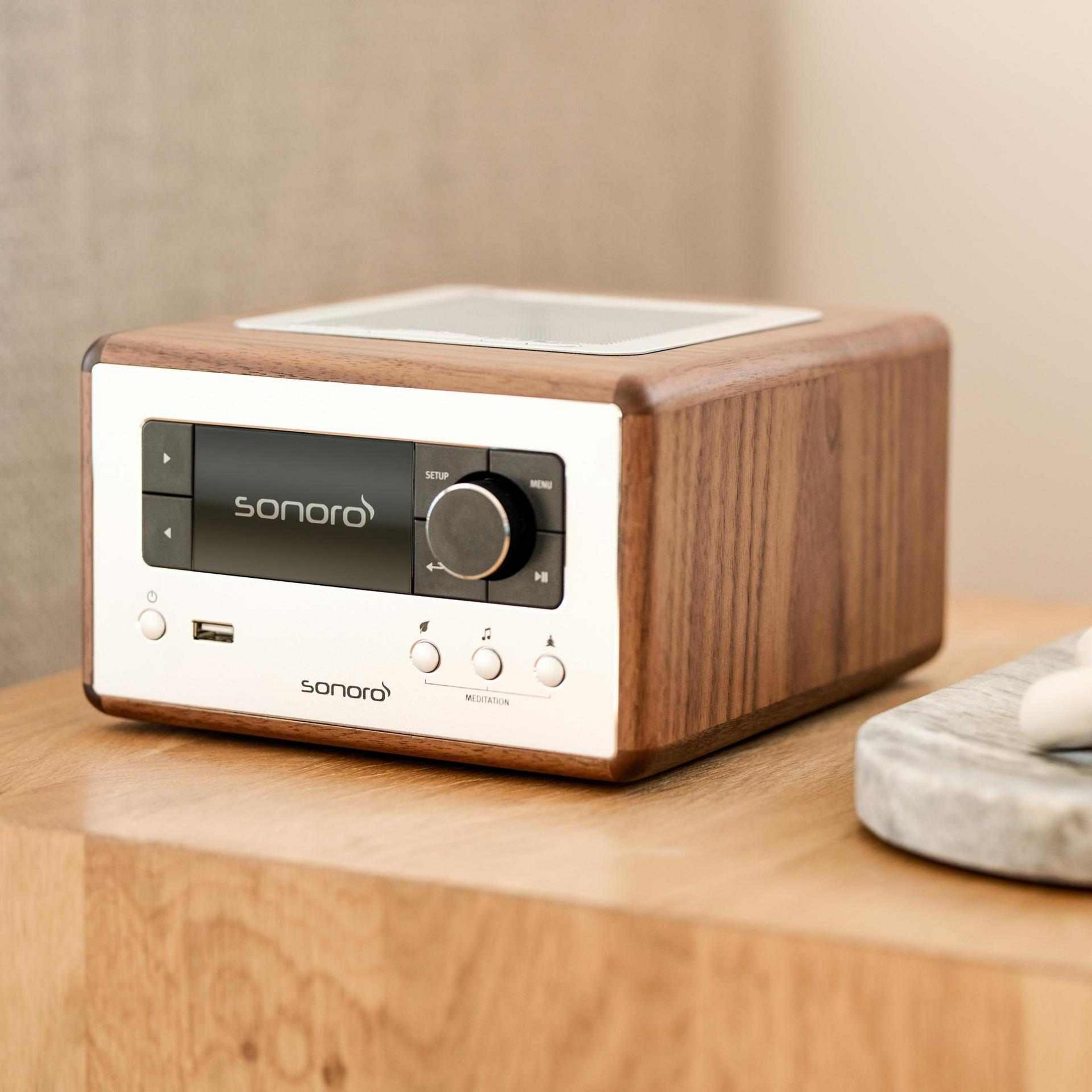 A wooden radio with a silver front and display sits on a wooden table.