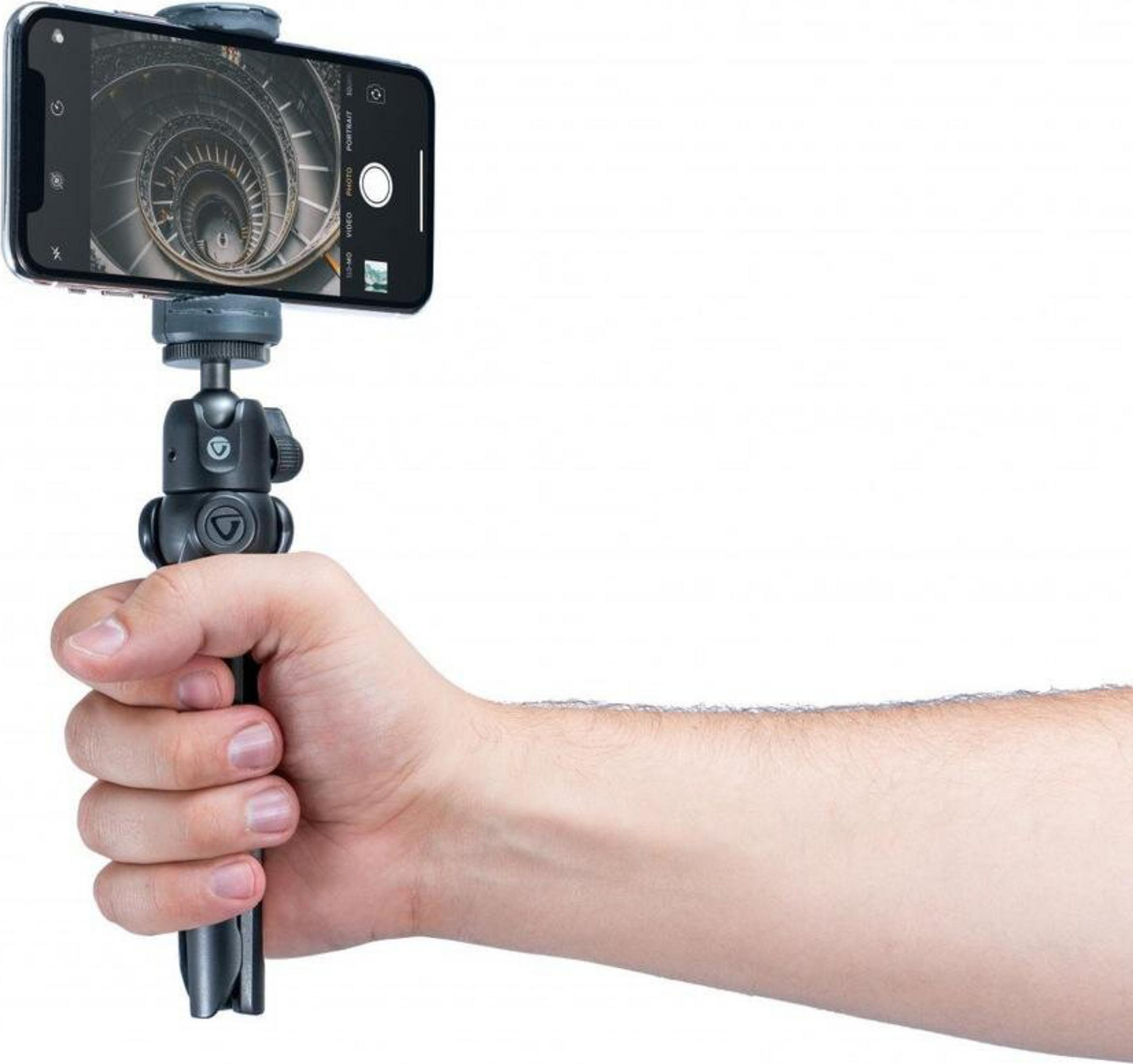 Una mano sostiene un smartphone en un trípode, filmando una escalera de caracol.