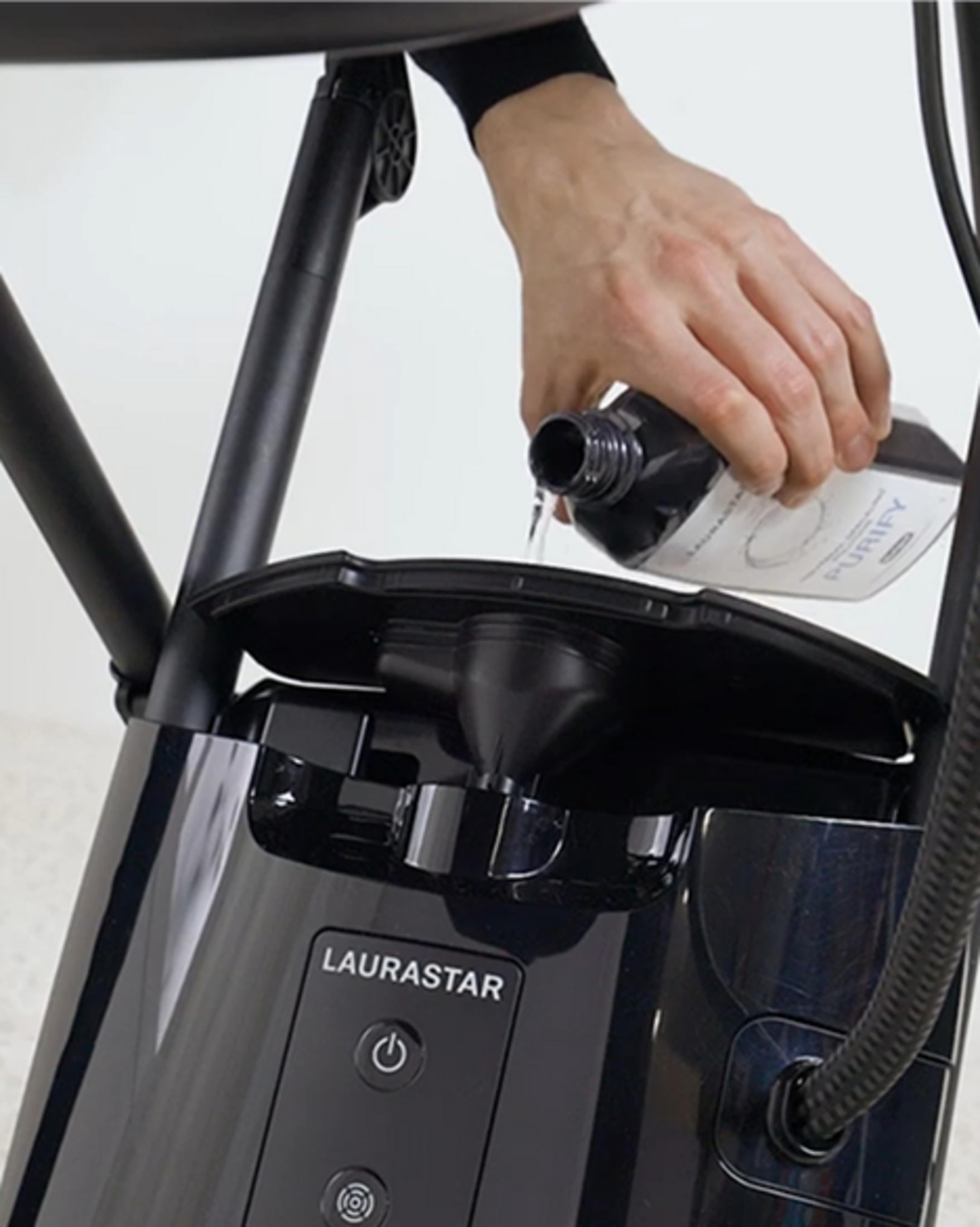 Eine Hand gießt Flüssigkeit aus einer Flasche in ein Gerät.