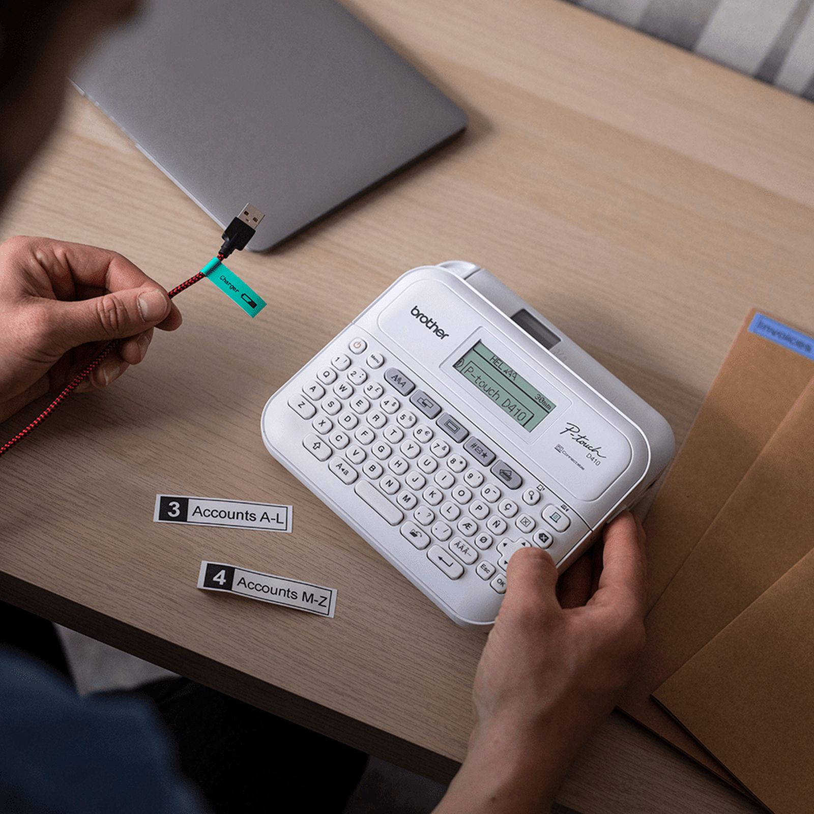 Ein Mann beschriftet Kabel mit einem Drucker. Laptop und Umschläge liegen auf dem Tisch.